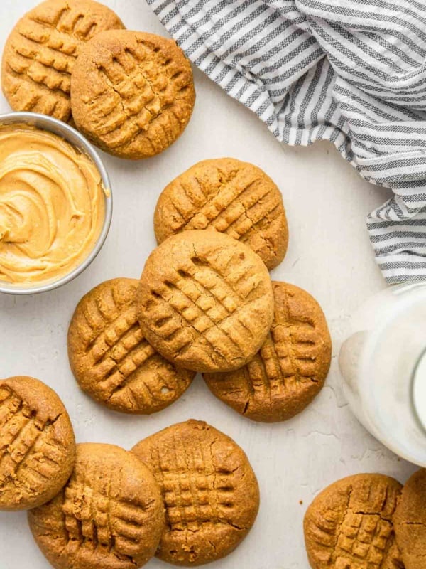 Criss cross 2 ingredient peanut butter cookies on white board with bowl of peanut butter.