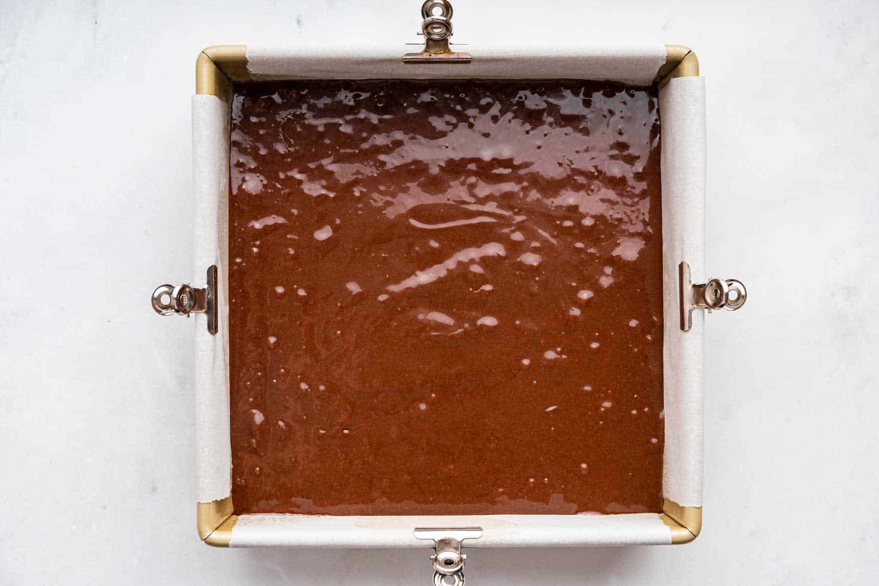 Raw brownie batter in a square pan before baking.