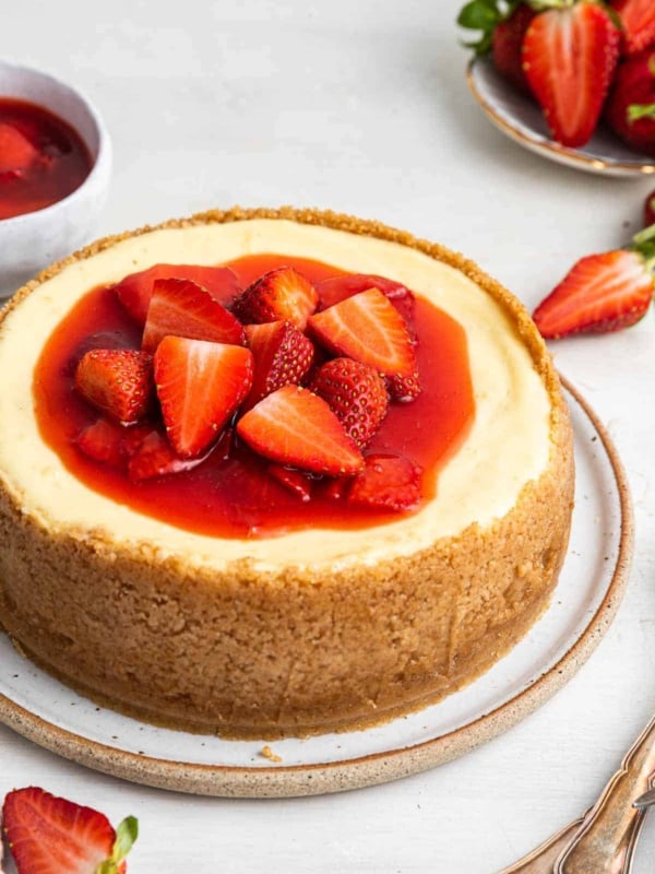 Small 6 inch cheesecake recipe with strawberry sauce on top and a tall crust.