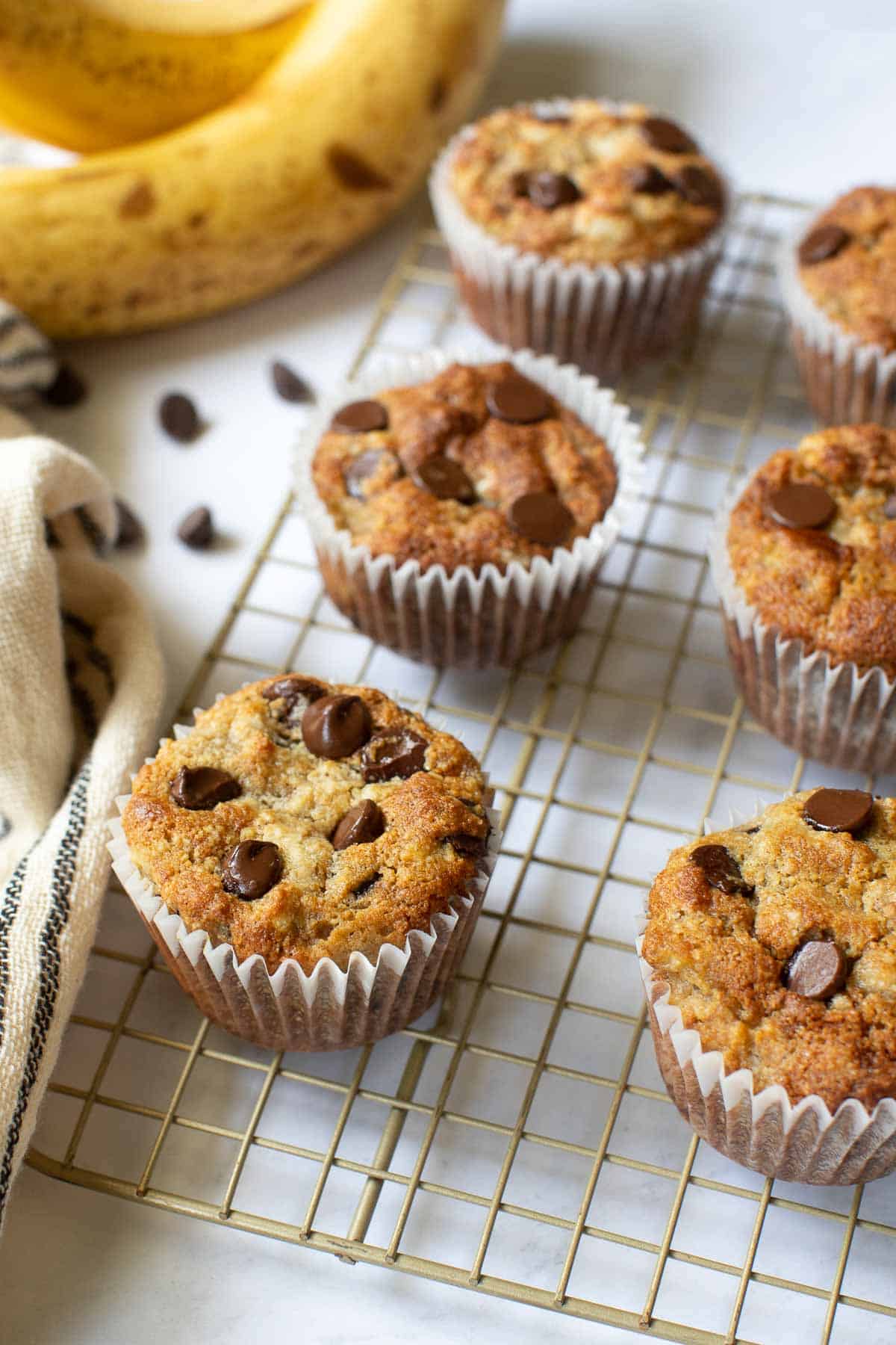 Six almond flour banana muffins with chocolate chips on wire rack.