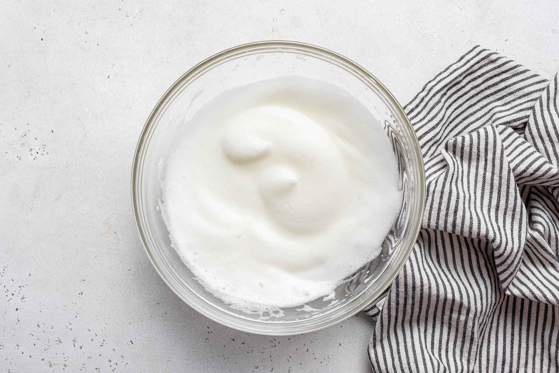 Whipped egg whites with soft peaks in bowl.