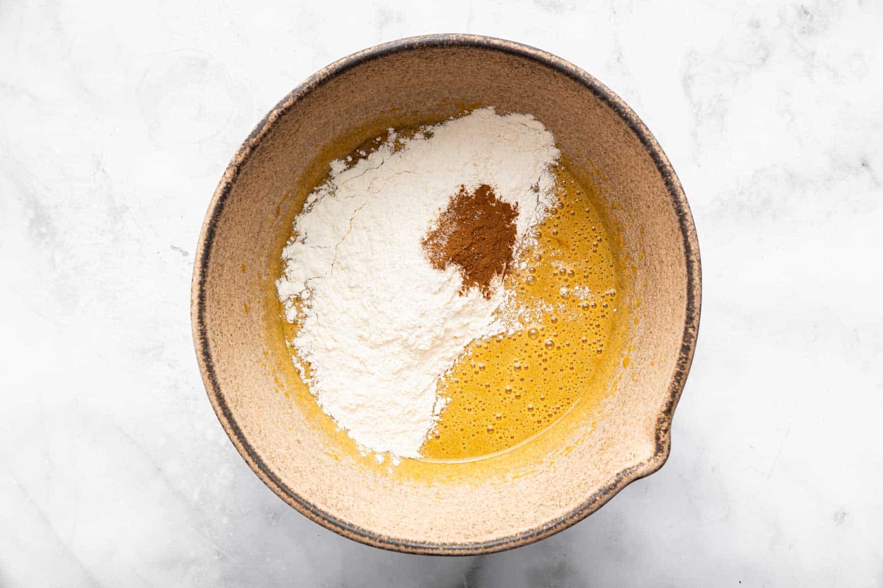 Brown bowl with yellow batter and white flour on top with cinnamon.