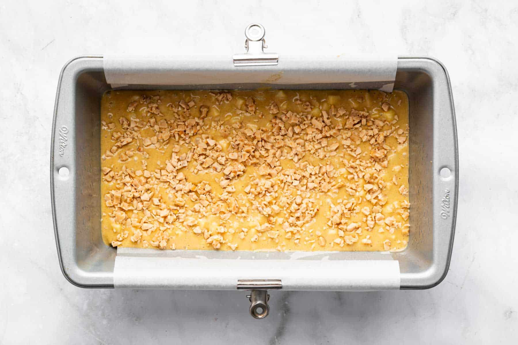 Tan batter in a loaf pan with toffee bits sprinkled on top.