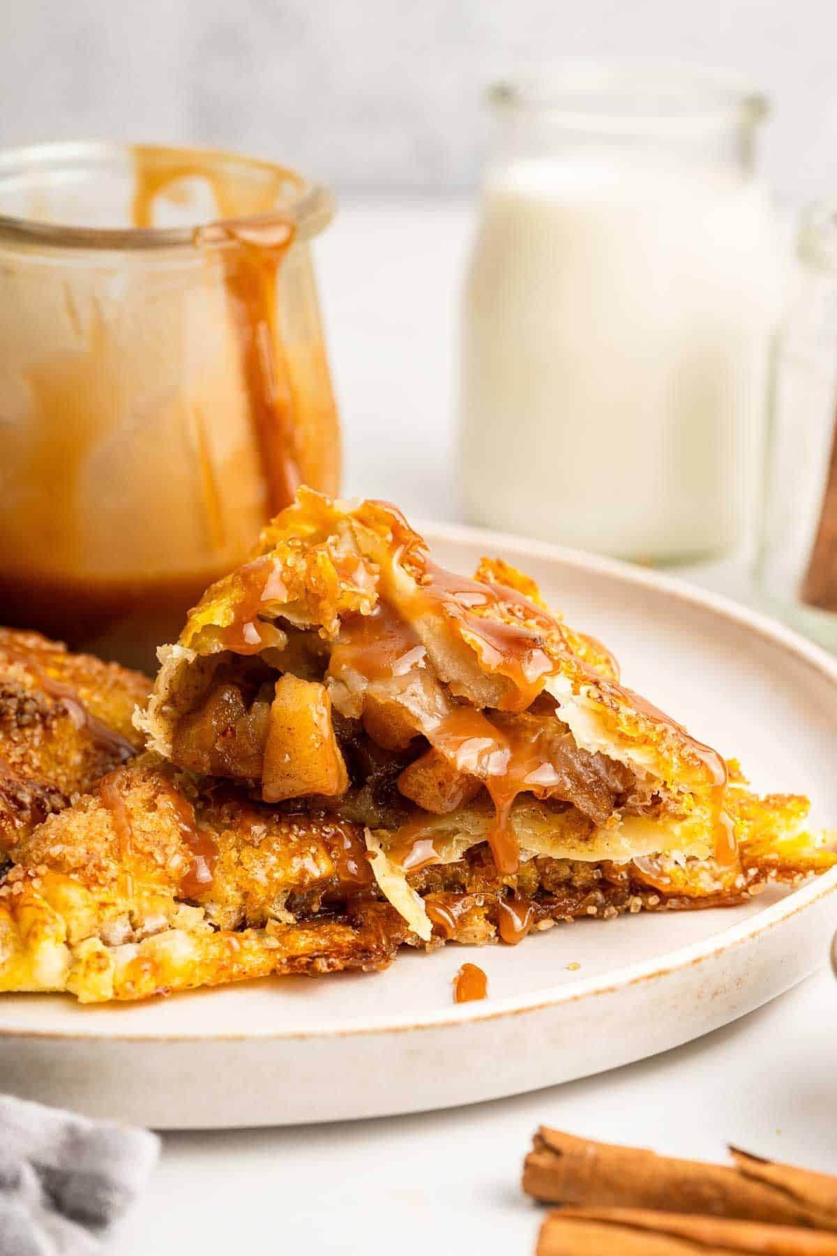 Golden brown apple turnovers on white plate with caramel cup in background.