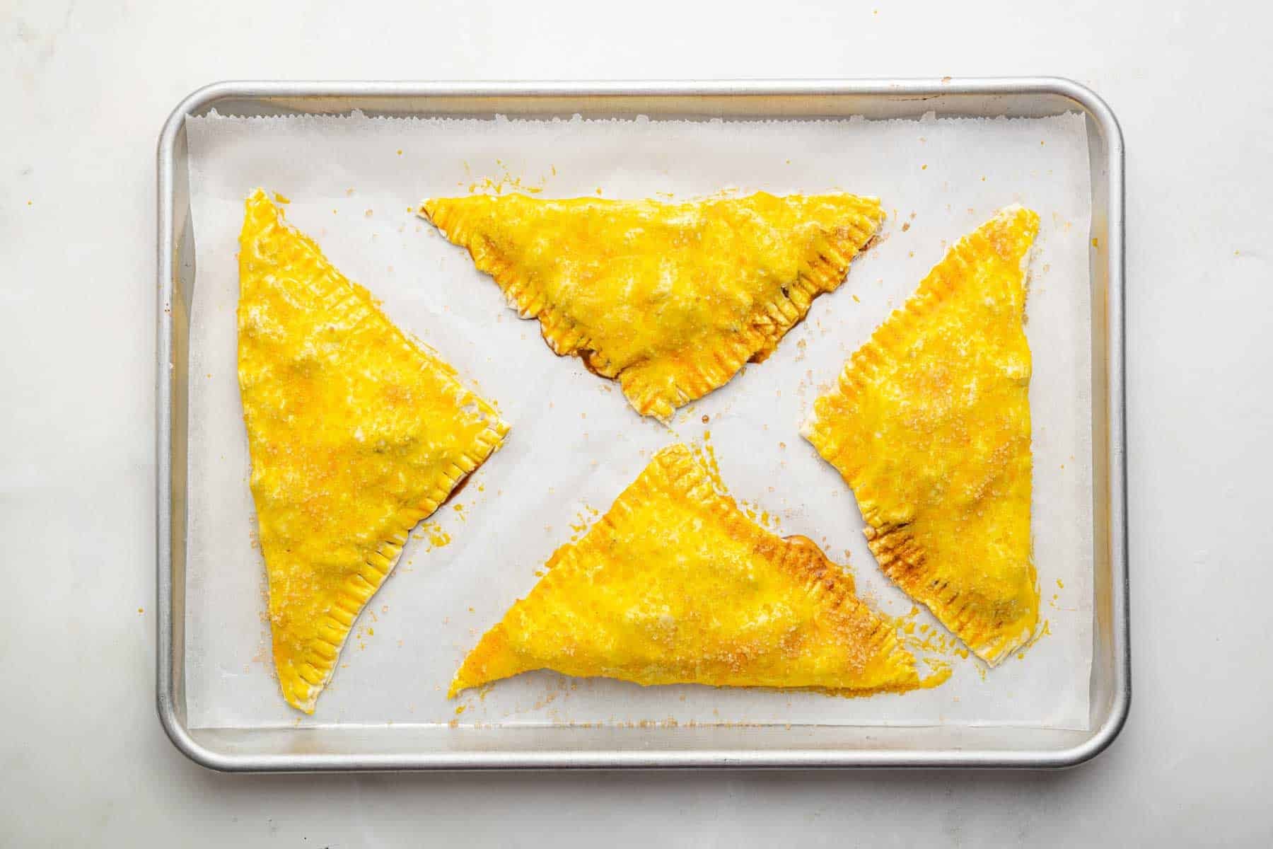 Four yellow triangles of pastry on a baking sheet.