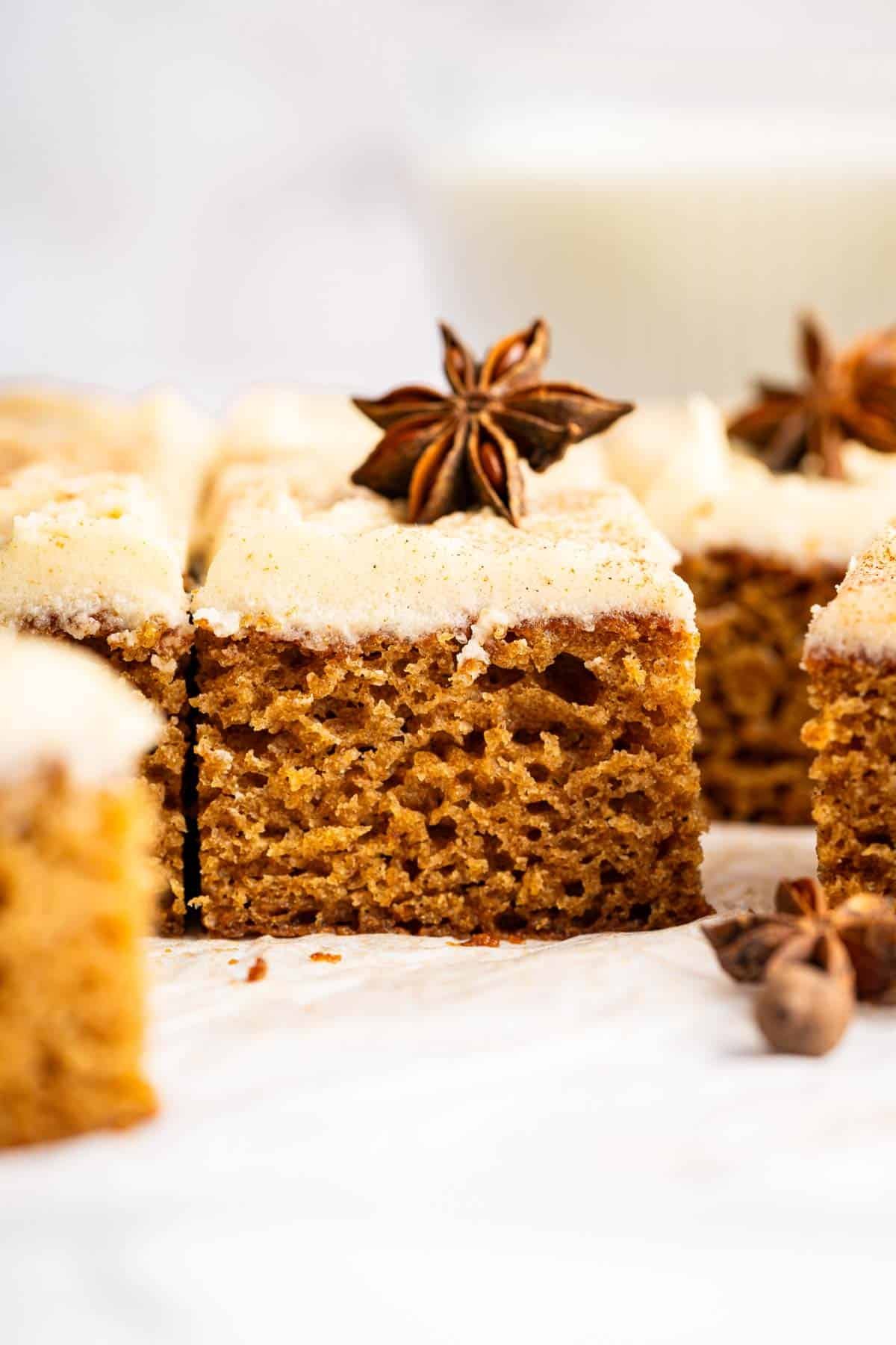 Square slice of applesauce cake with white frosting and star anise on top.