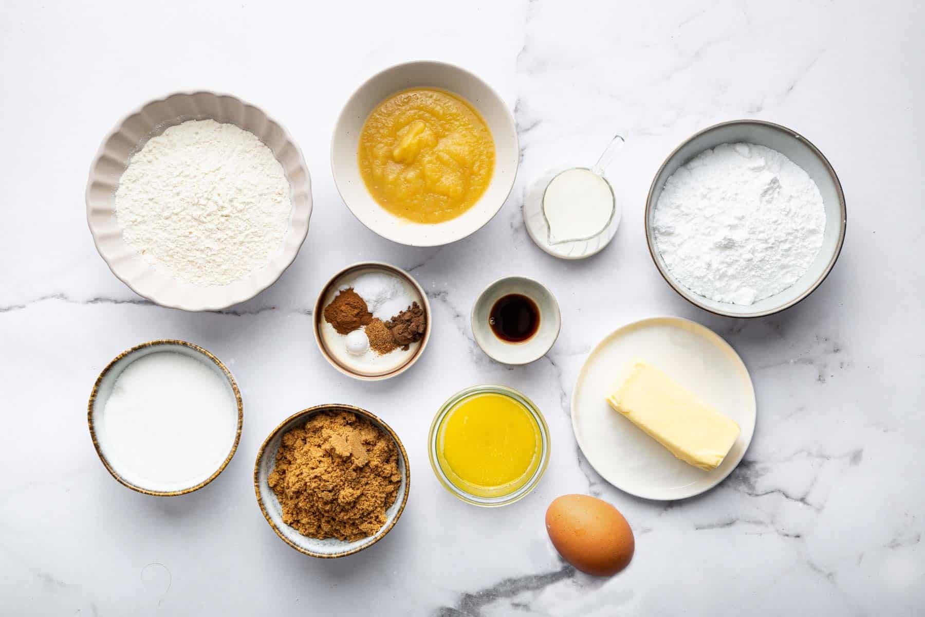 Bowls of baking ingredients, like sugar, eg, and melted butter on a kitchen table.