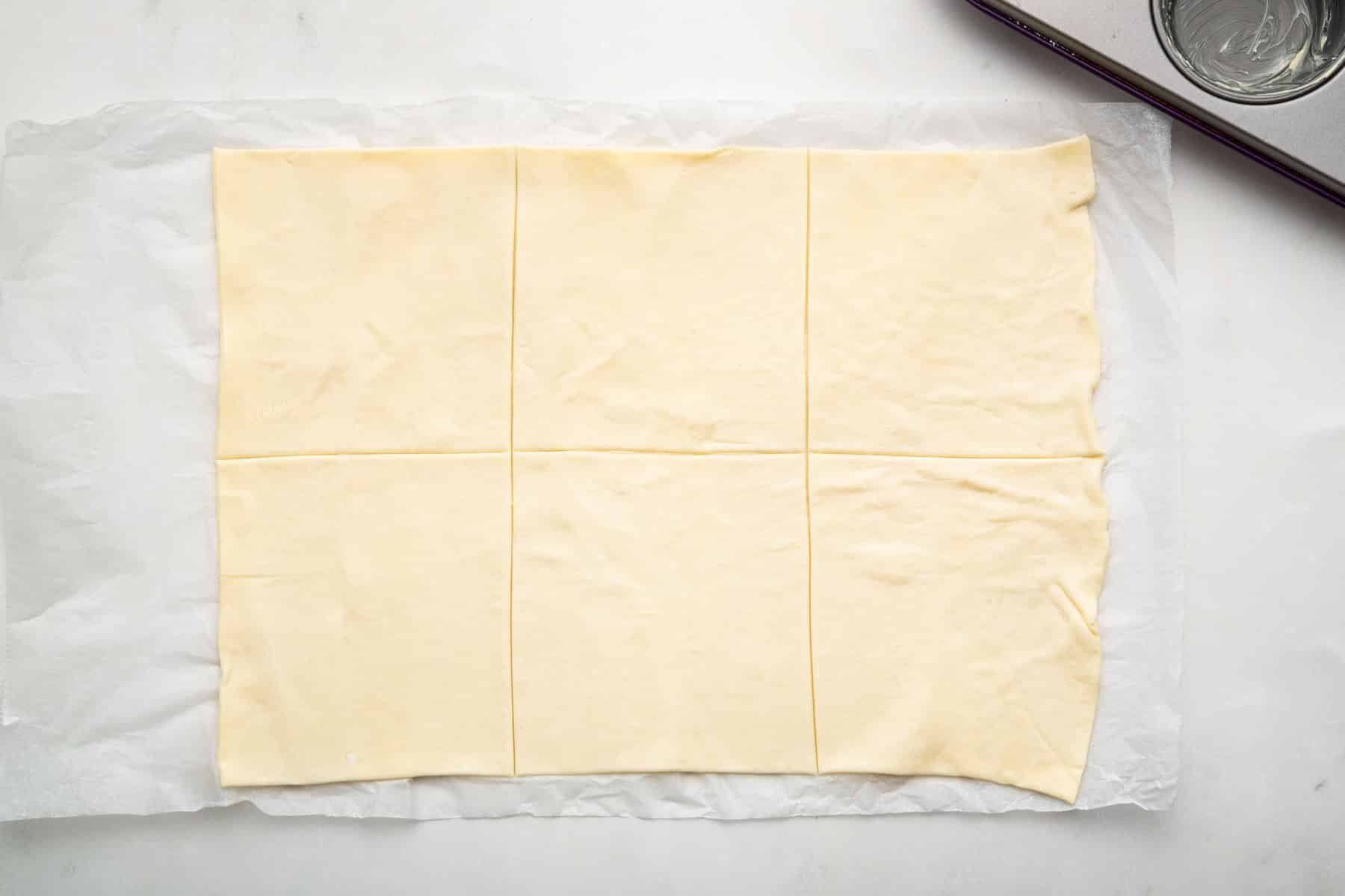 Sheet of puff pastry on counter cut into 6 squares.