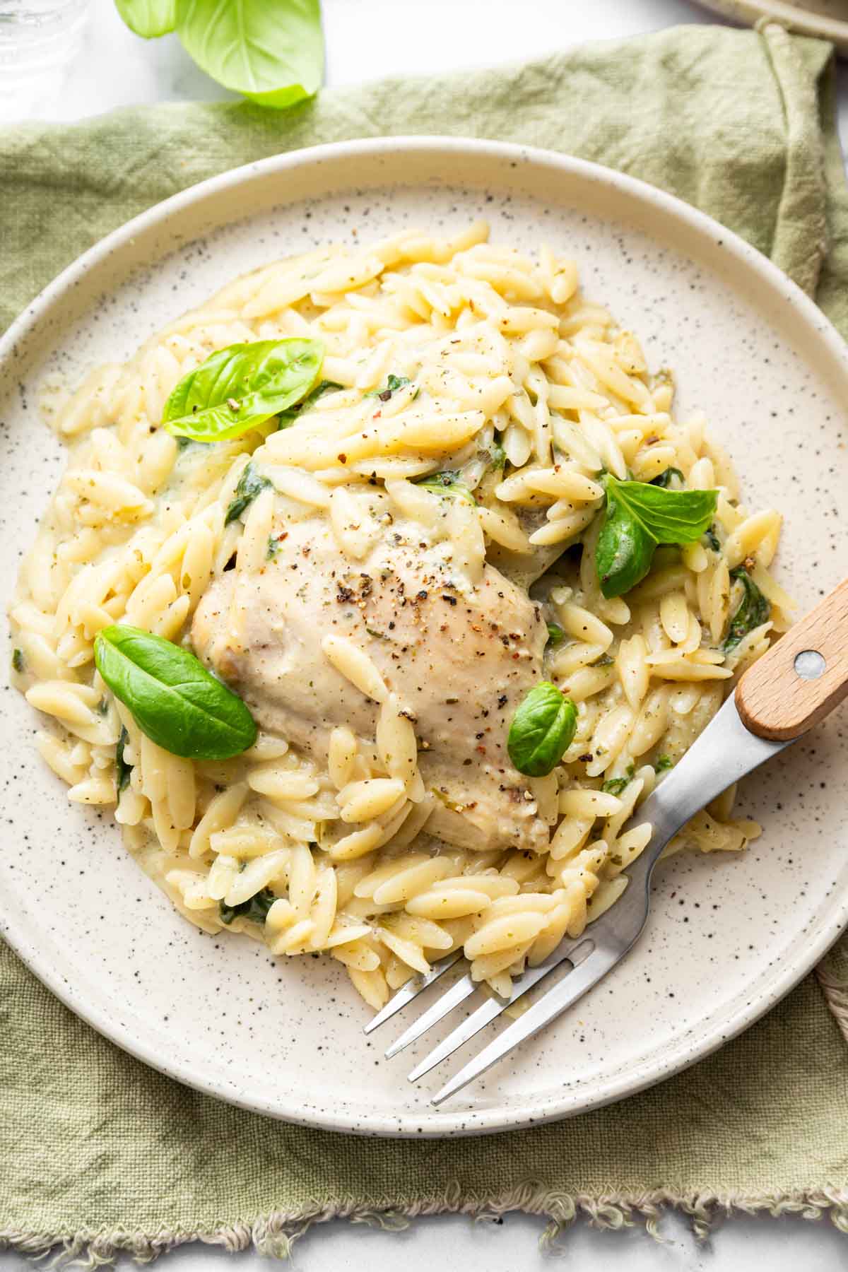 Single serving of baked chicken orzo on plate garnished with basil.