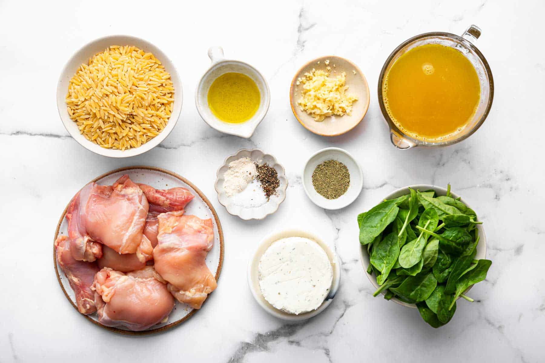 Small bowls of pasta, broth, spinach, and spices on kitchen counter.