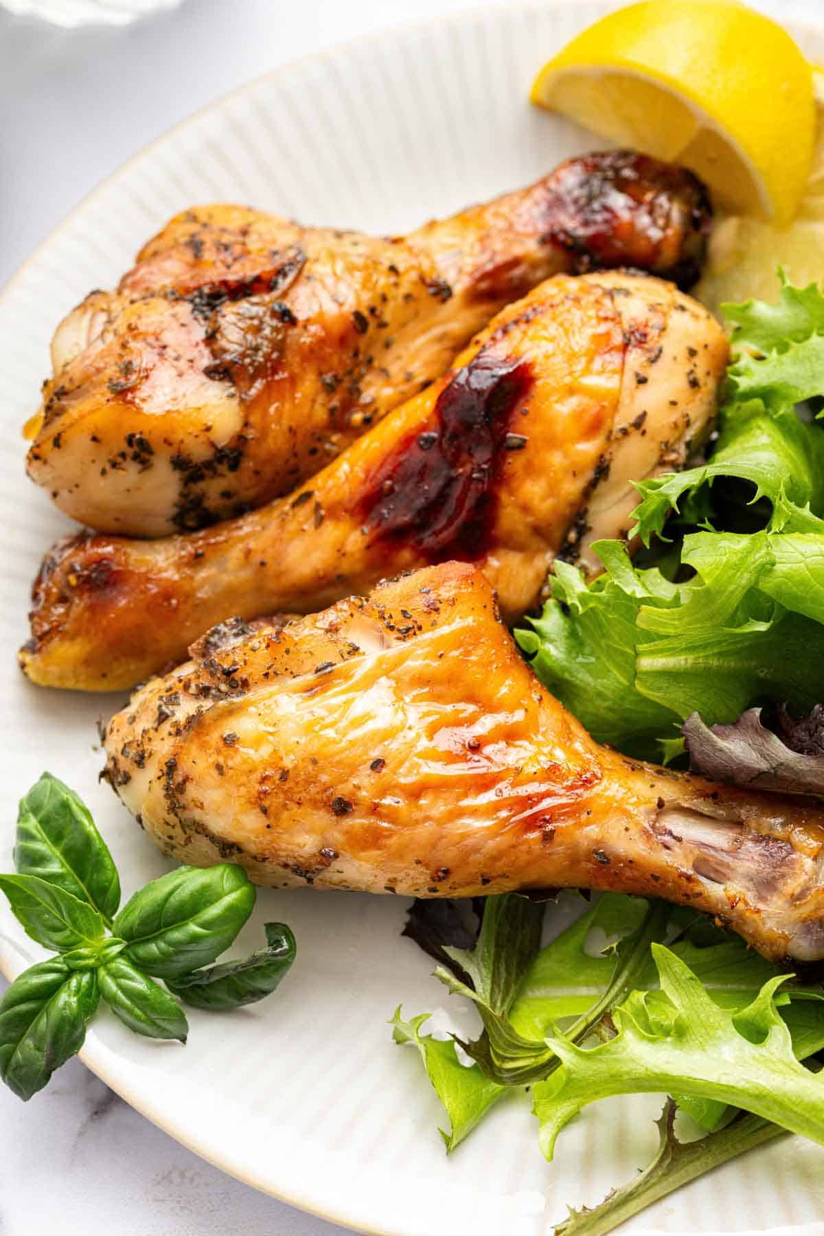 Chicken drumsticks on a plate with salad greens and lemon wedges.
