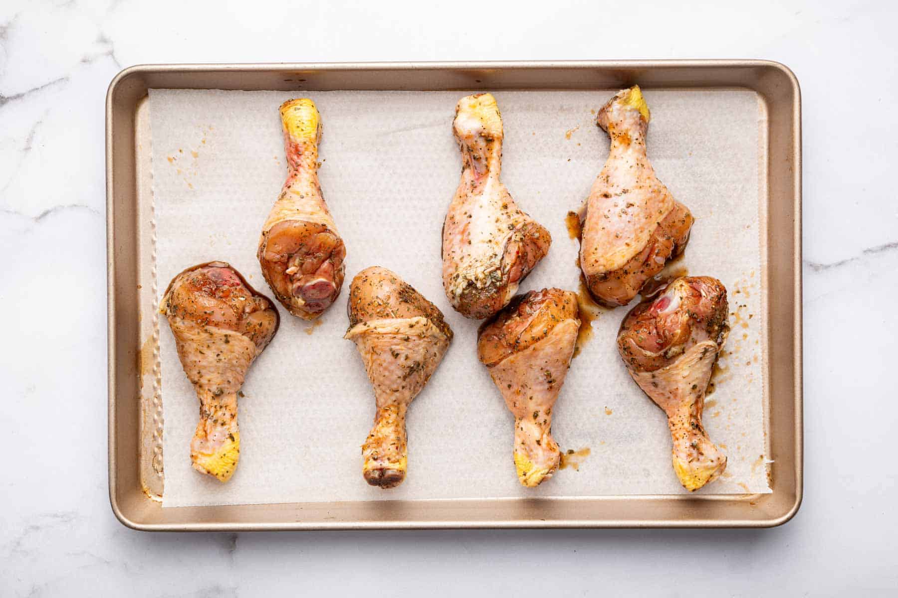 Marinated raw chicken drumsticks on a sheet pan lined with parchment.