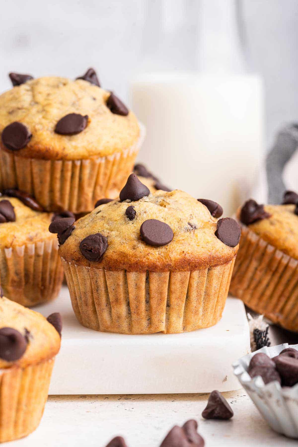 Six banana chocolate chip muffins on white cutting board with milk in background.