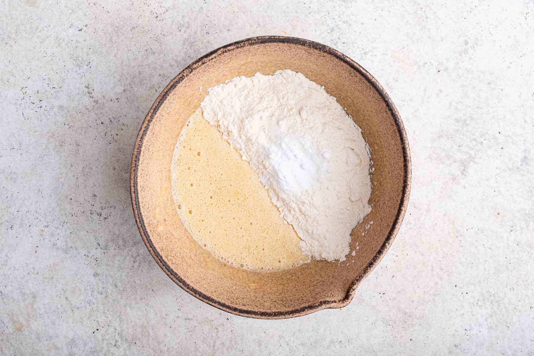 Flour on top of yellow batter in brown bowl.