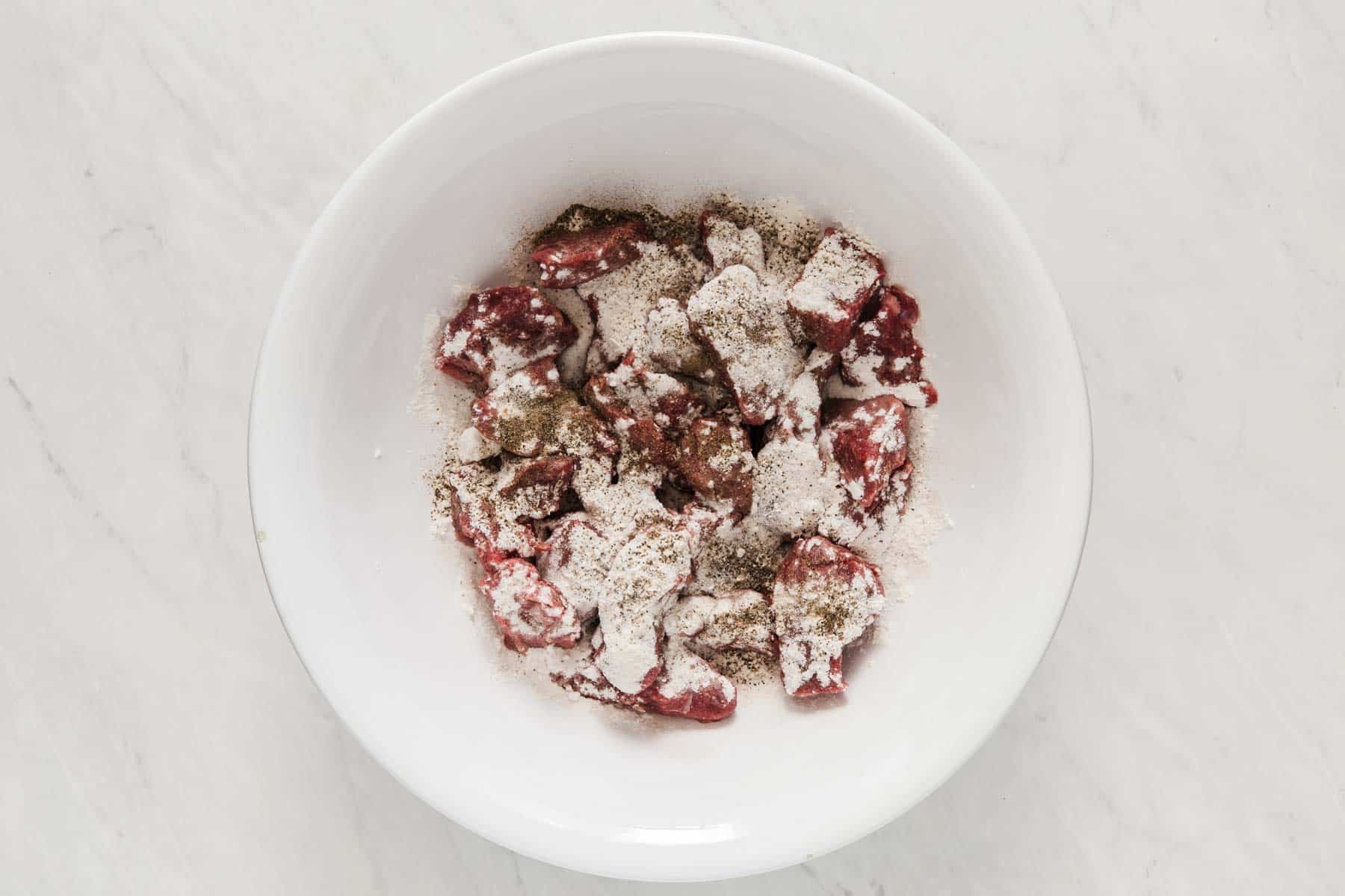 White bowl with flour coated red meat inside.