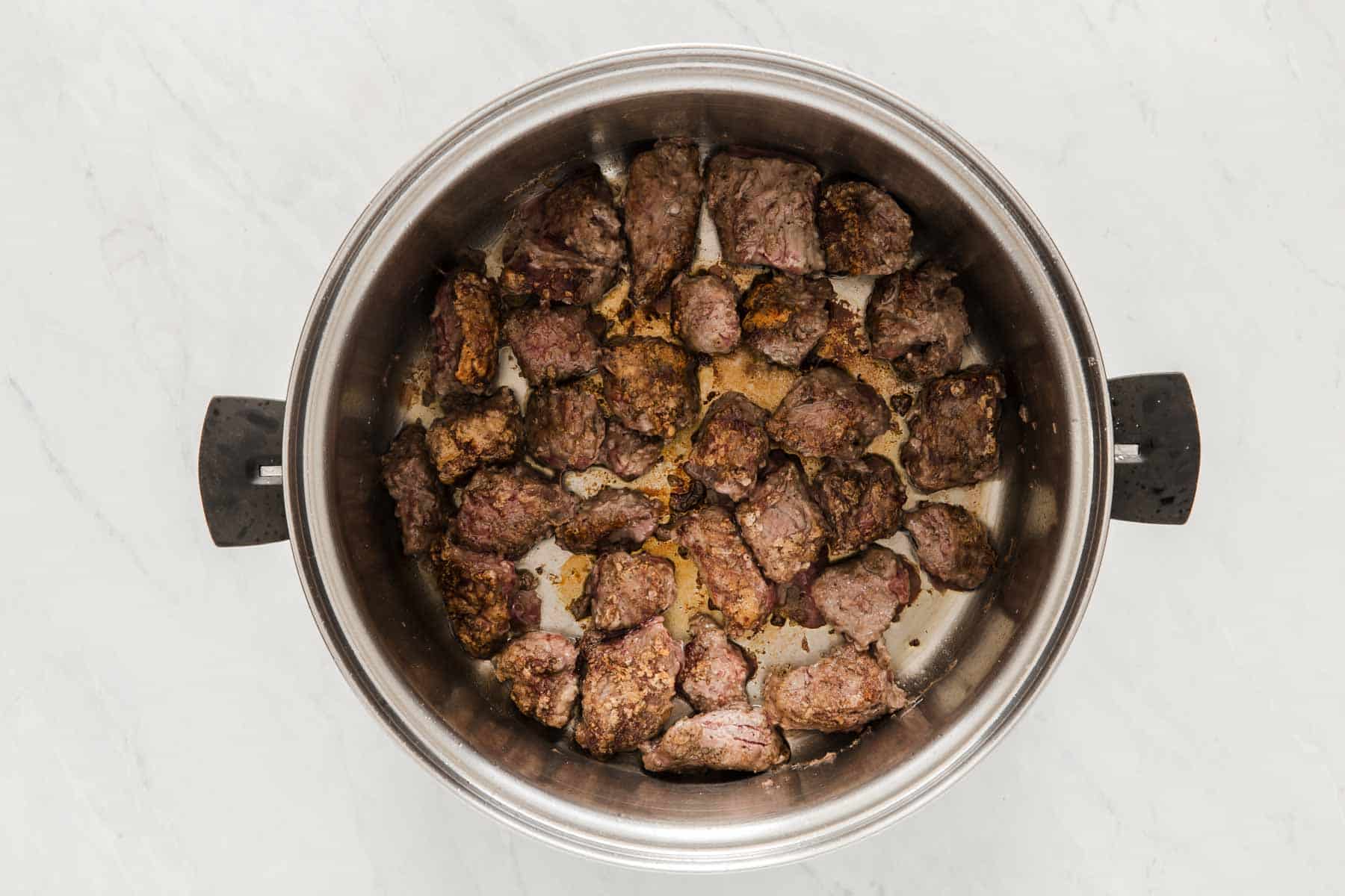 Meat being seared in a round metal pan.