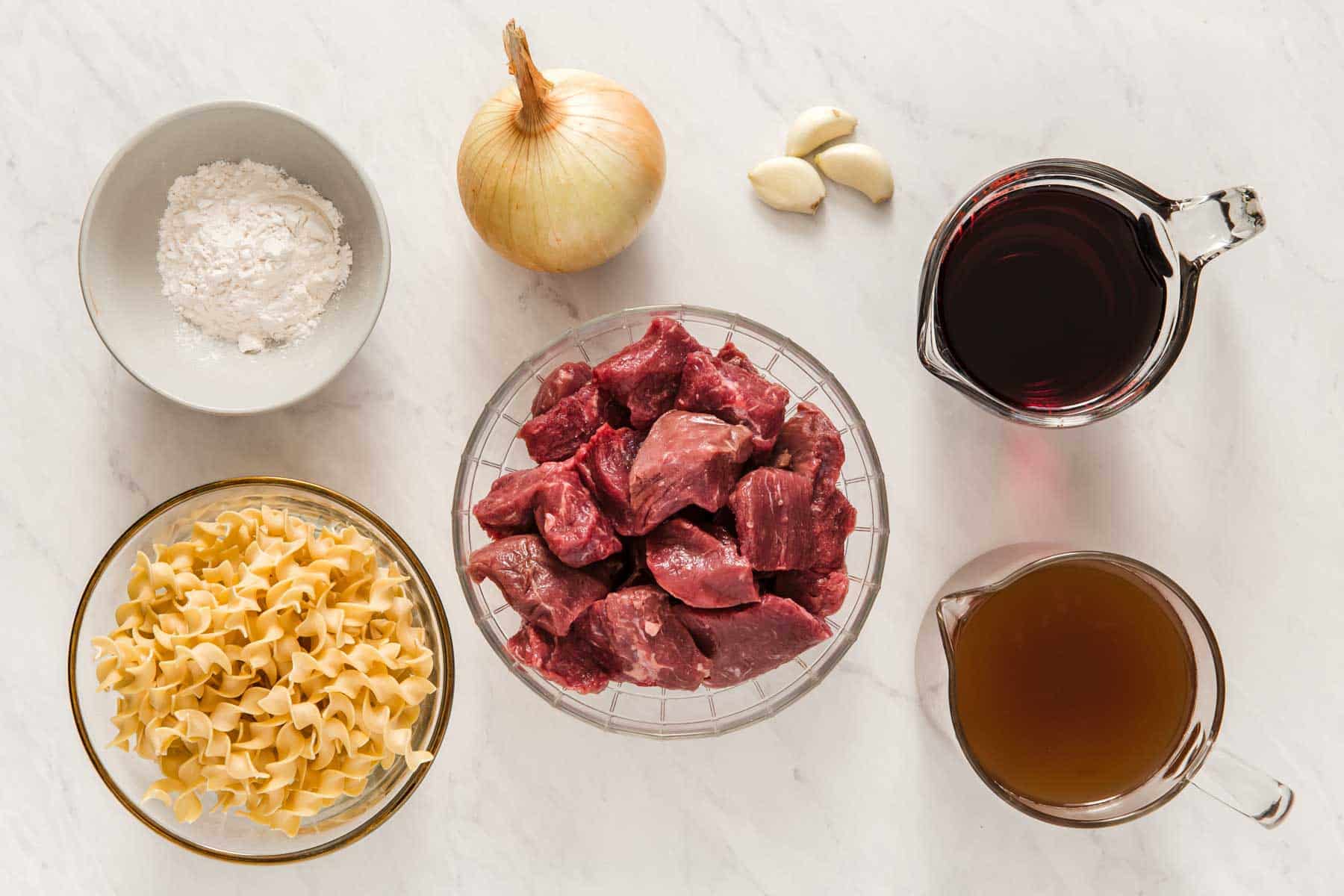 Bowl of chopped red meat, pasta, onion, and broth on kitchen counter.
