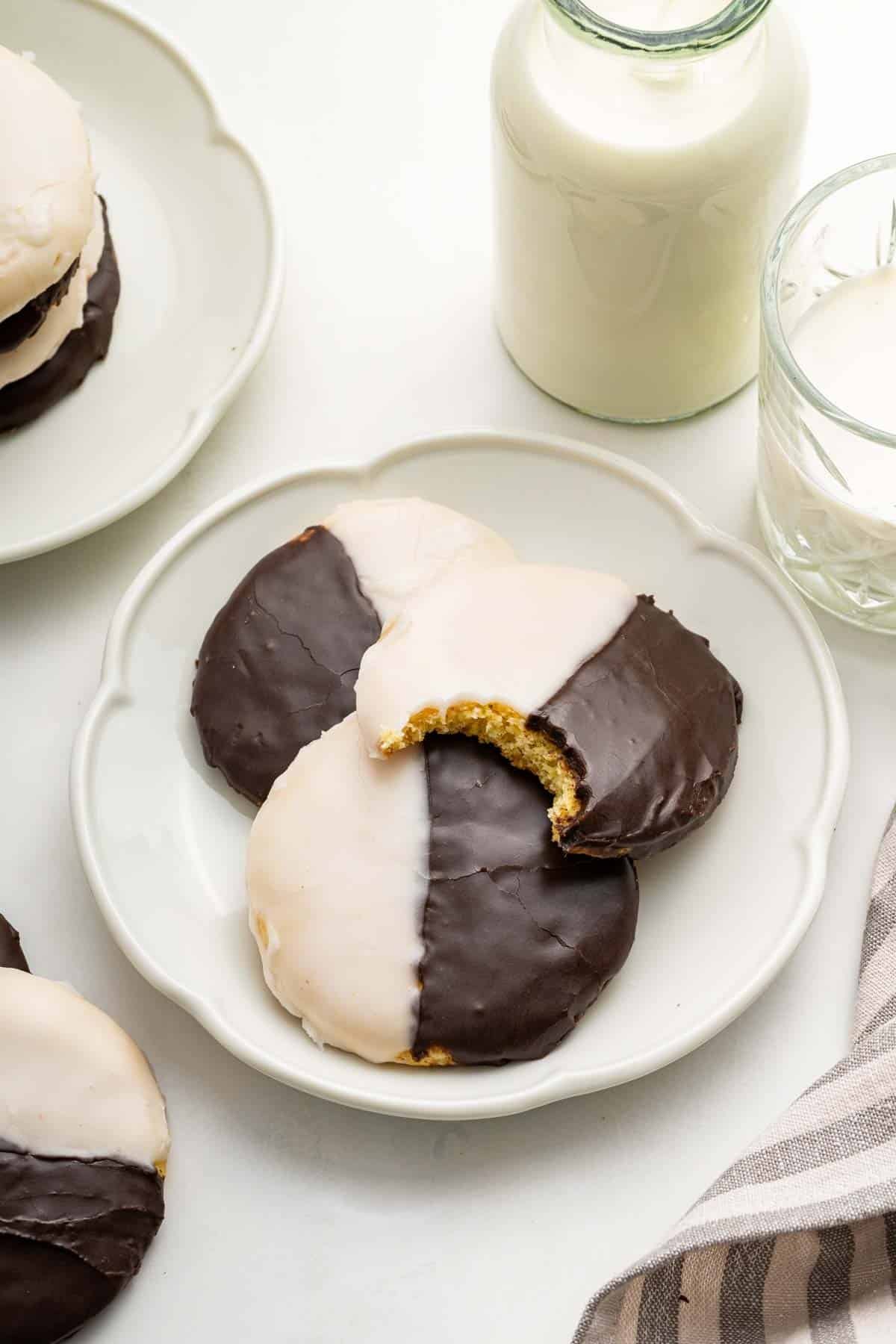 Three black and white cookies on a white plate with milk on the side.