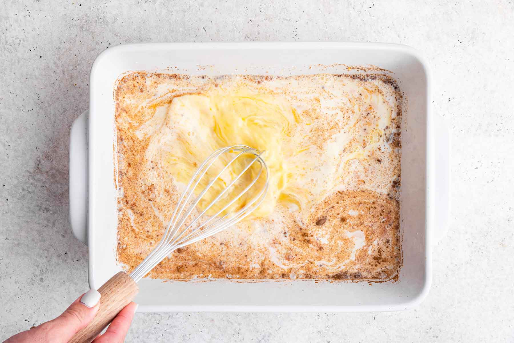 Hand whisking custard together in rectangular dish.