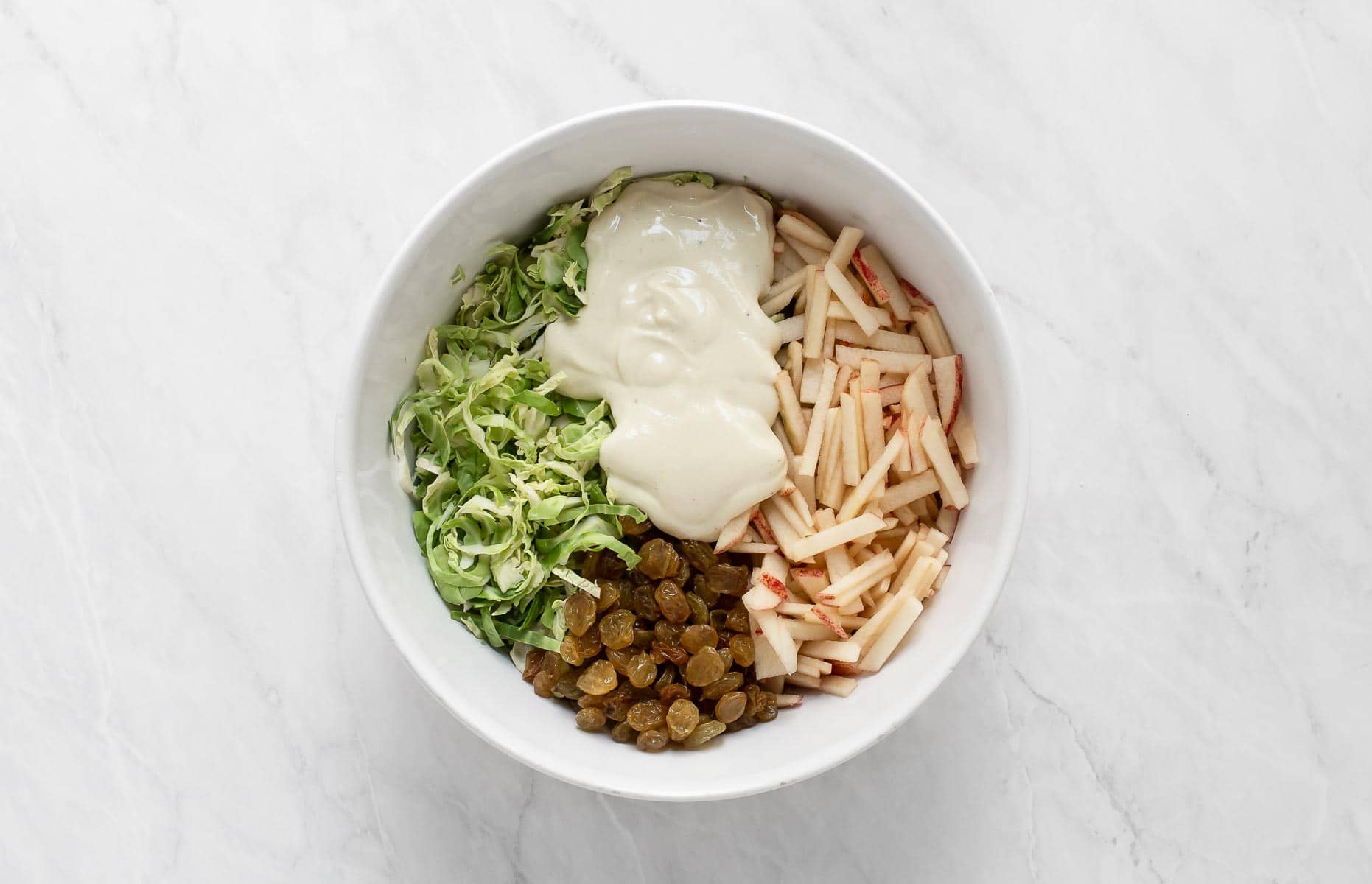 Brussels sprout slaw in bowl with dressing on top.
