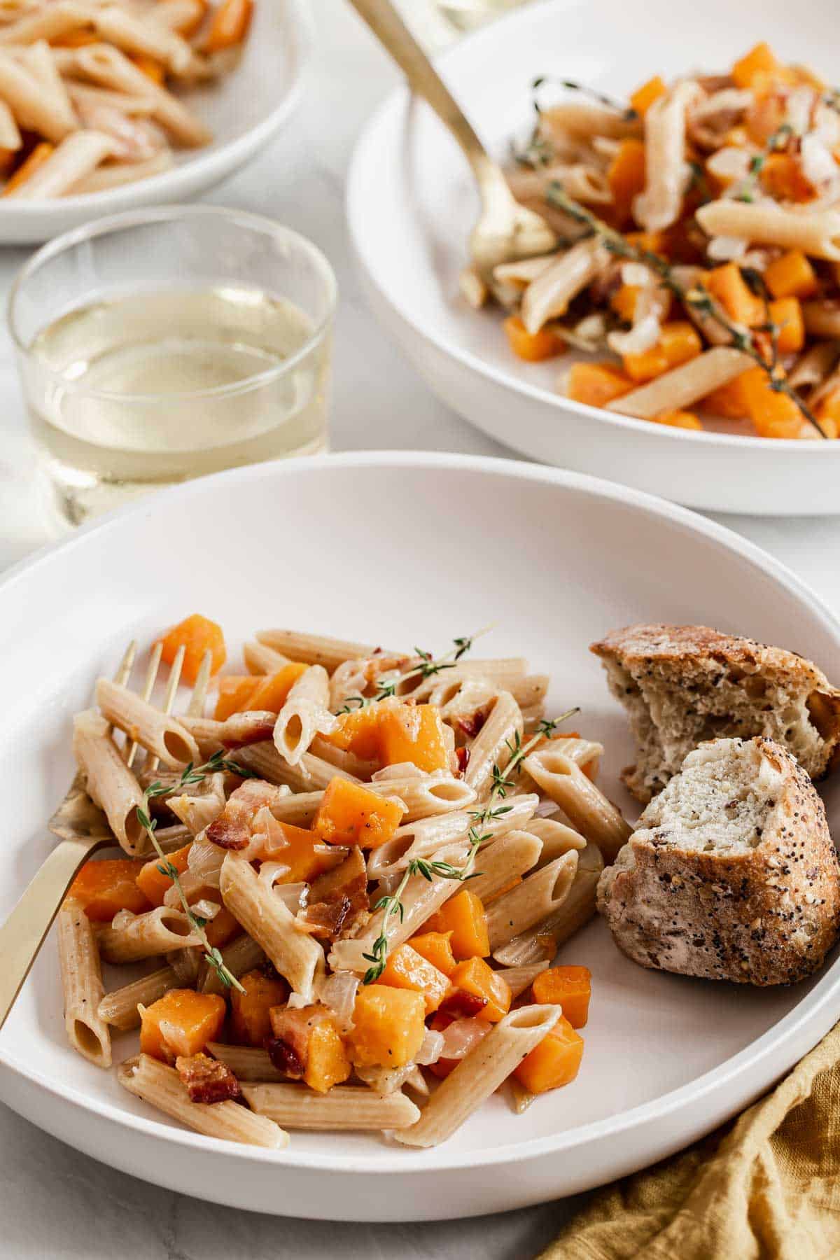 Two bowl of pasta with butternut squash cubes and bread on the side.