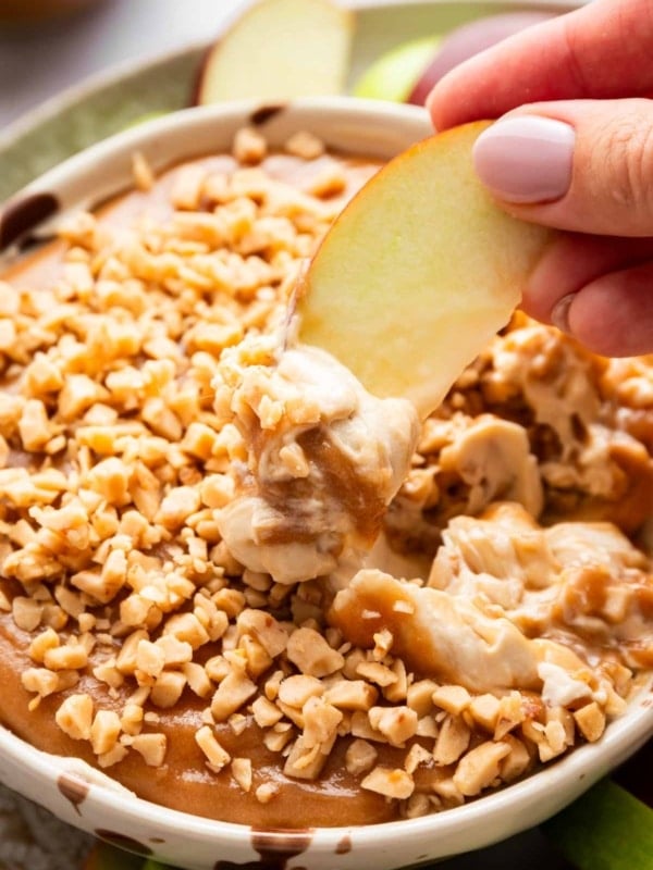 Red apple slice being dragged through caramel apple fruit dip.