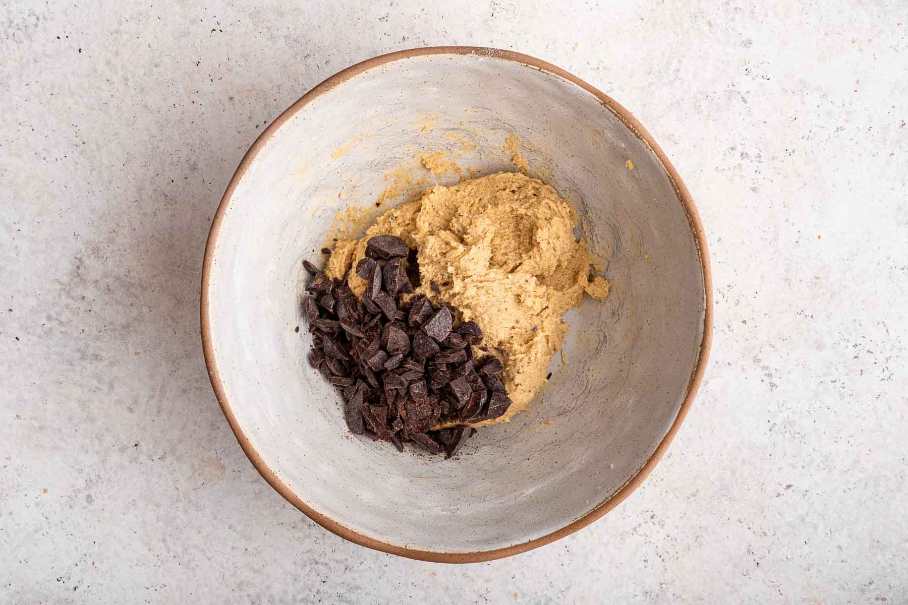 Chopped chocolate in bowl of cookie dough.