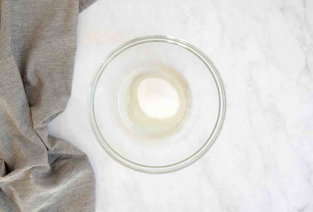 Clear bowl with oil and sugar and kitchen towel on side.