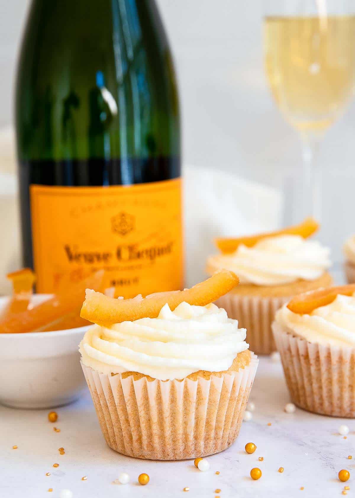 White cupcakes with champagne bottle in background.