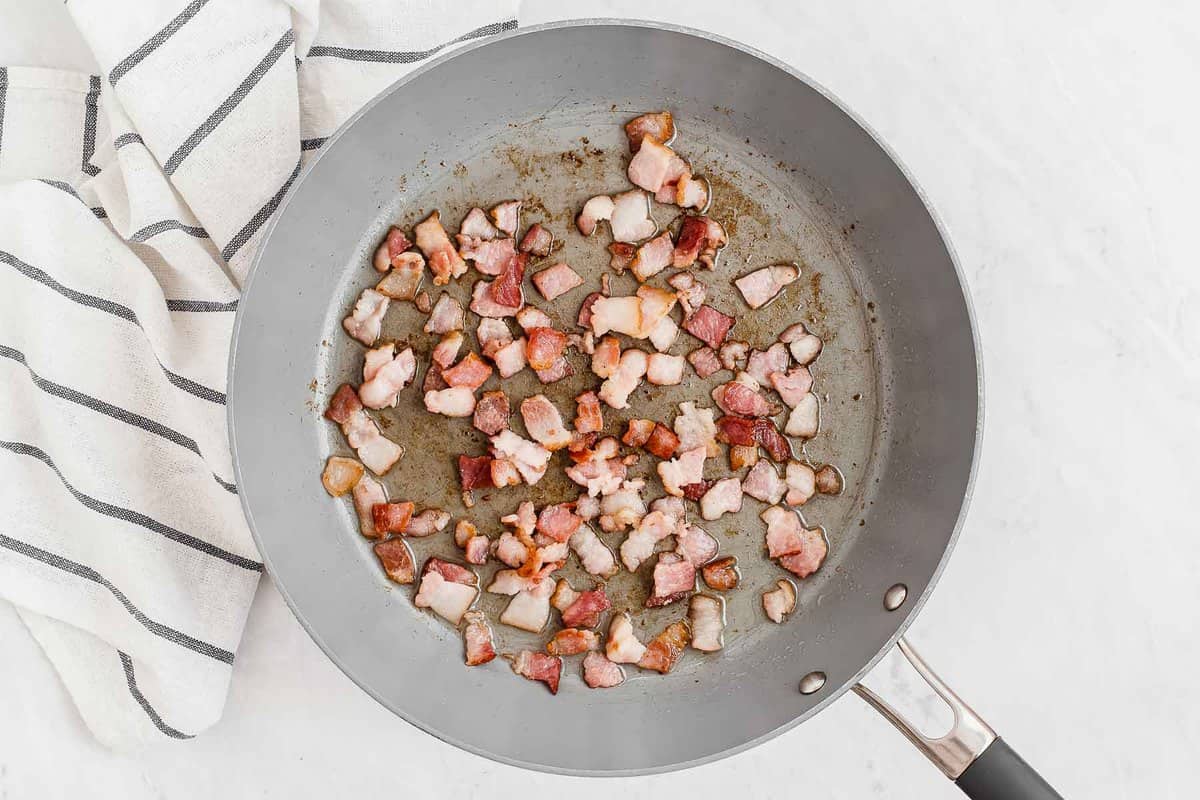 bacon pieces cooking in a grey skillet