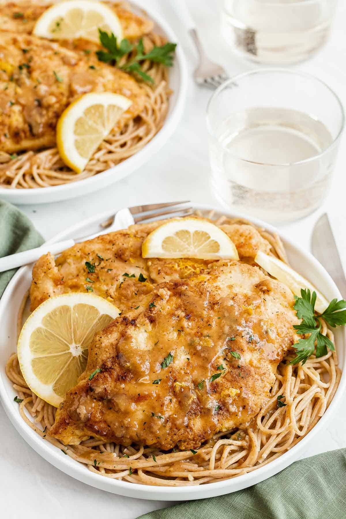 Two plates with chicken over pasta with a lemon garnish.