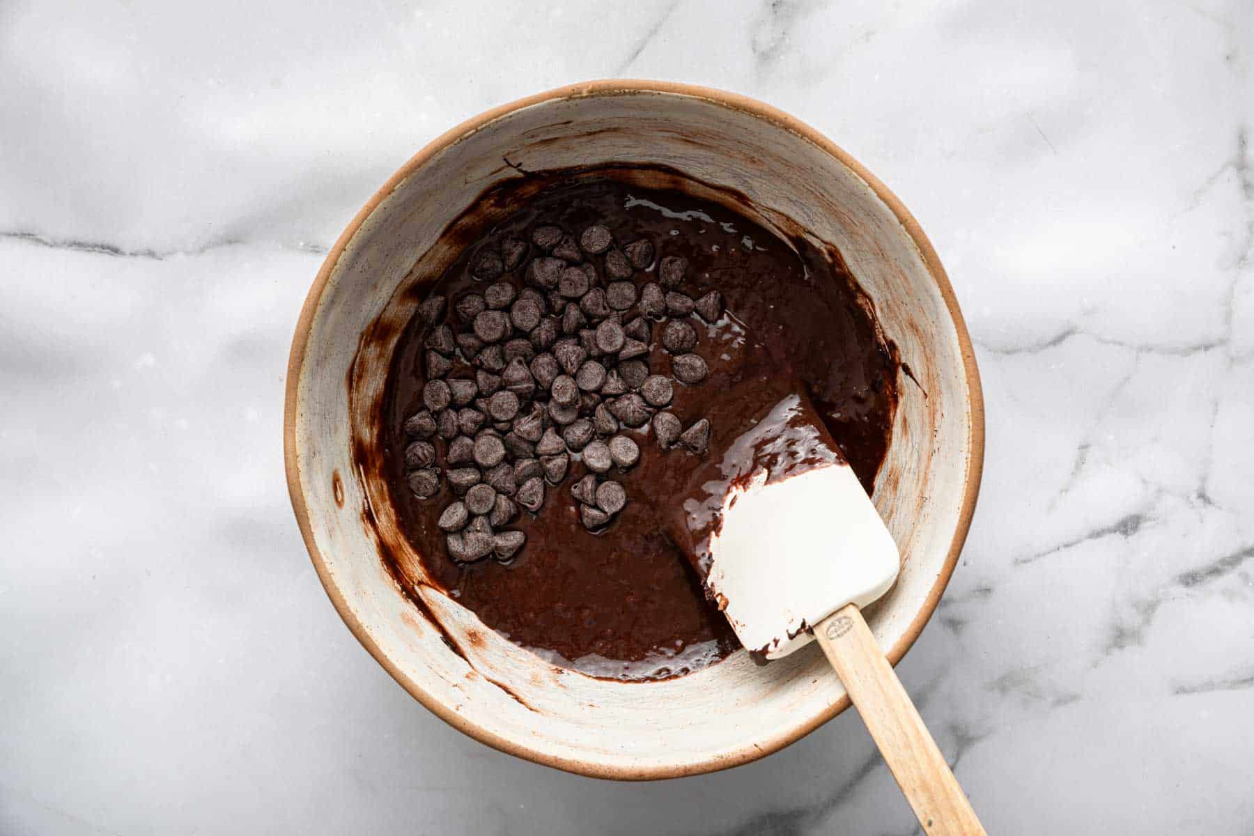 Rich dark brown chocolate banana muffin batter with pile of chocolate chips on top.