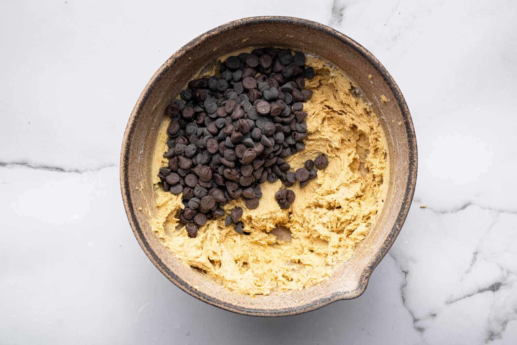 Yellow dough with chocolate chips on top in bowl.
