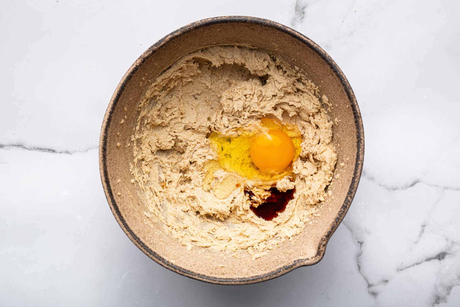 Brown dough with egg cracked on top with splash of vanilla.