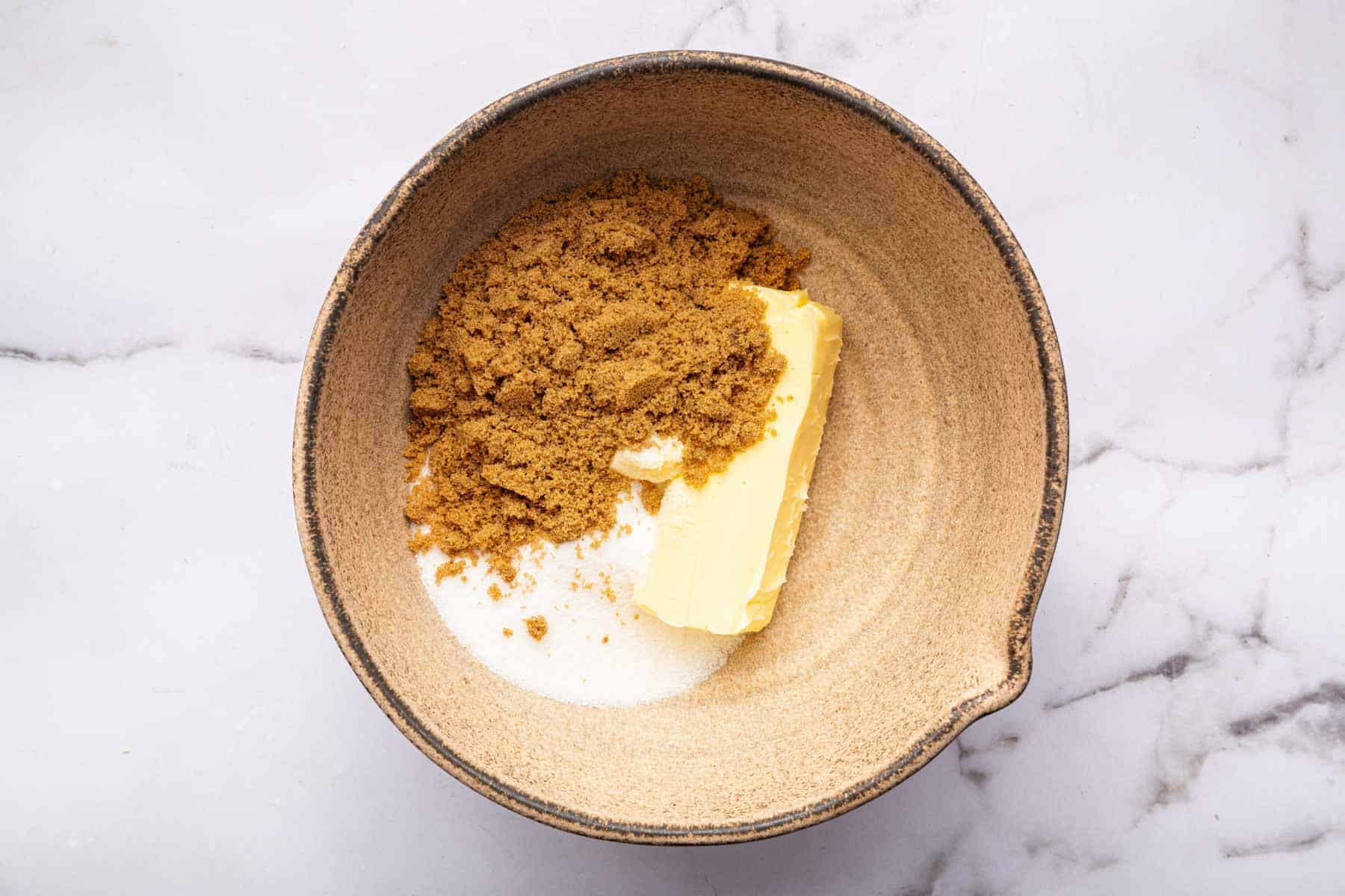Brown bowl with butter, brown sugar, and white sugar.