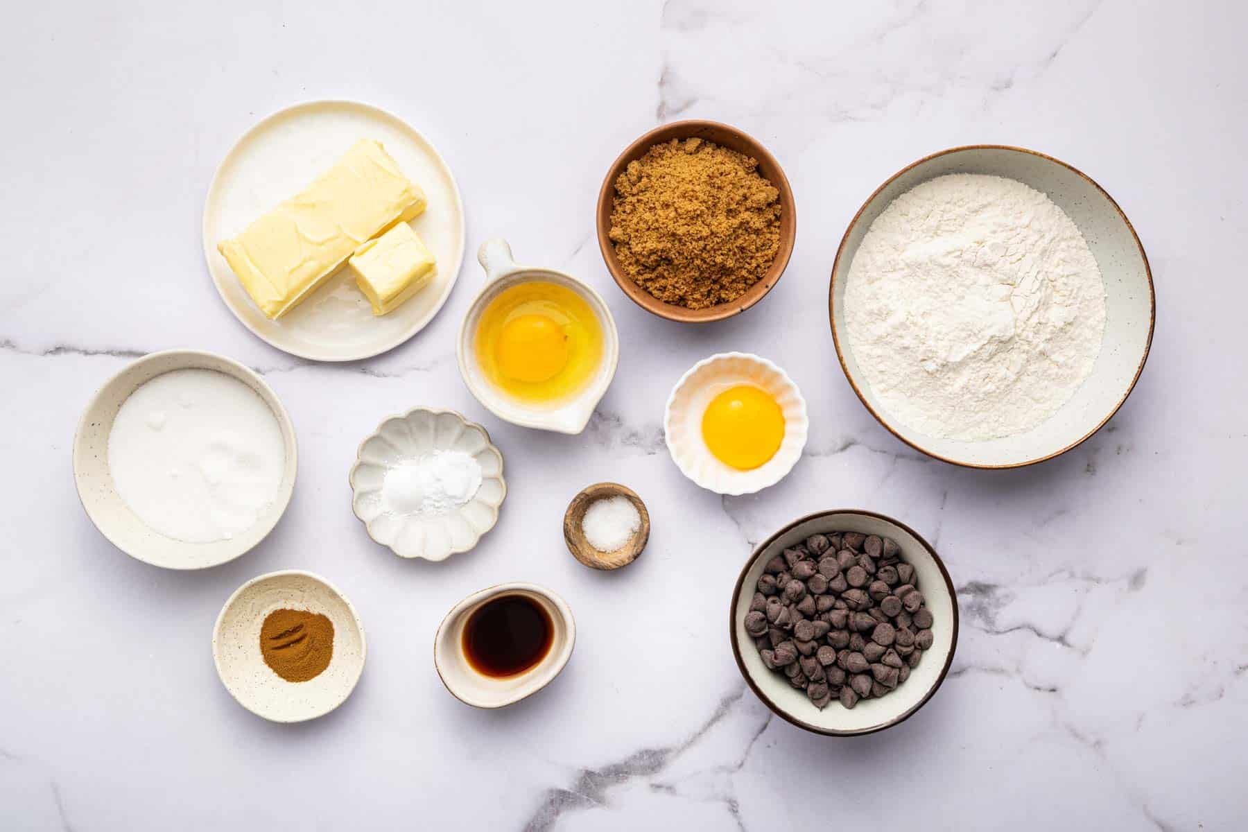 Small white bowls with baking ingredients like sugar, chocolate, and flour.
