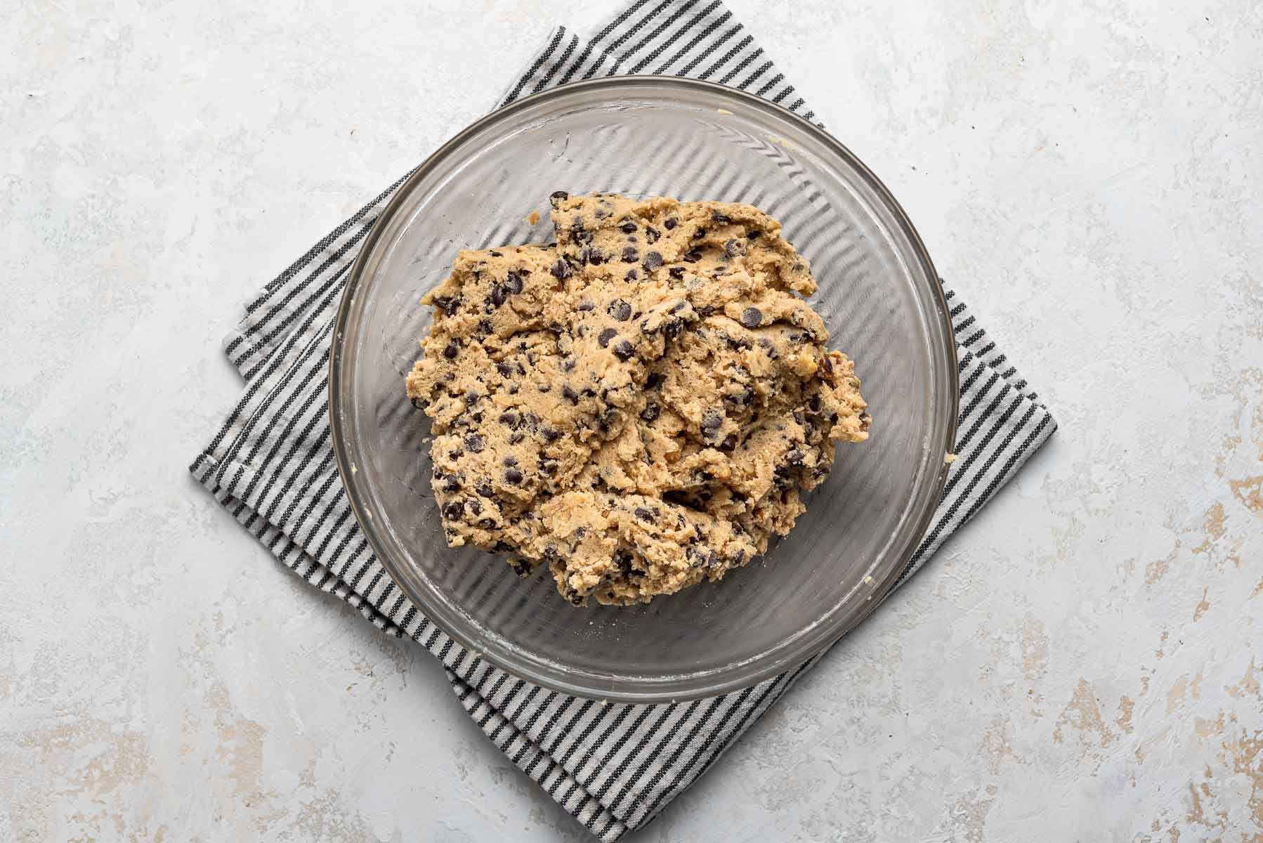 Raw cookie dough in clear bowl with kitchen towel.