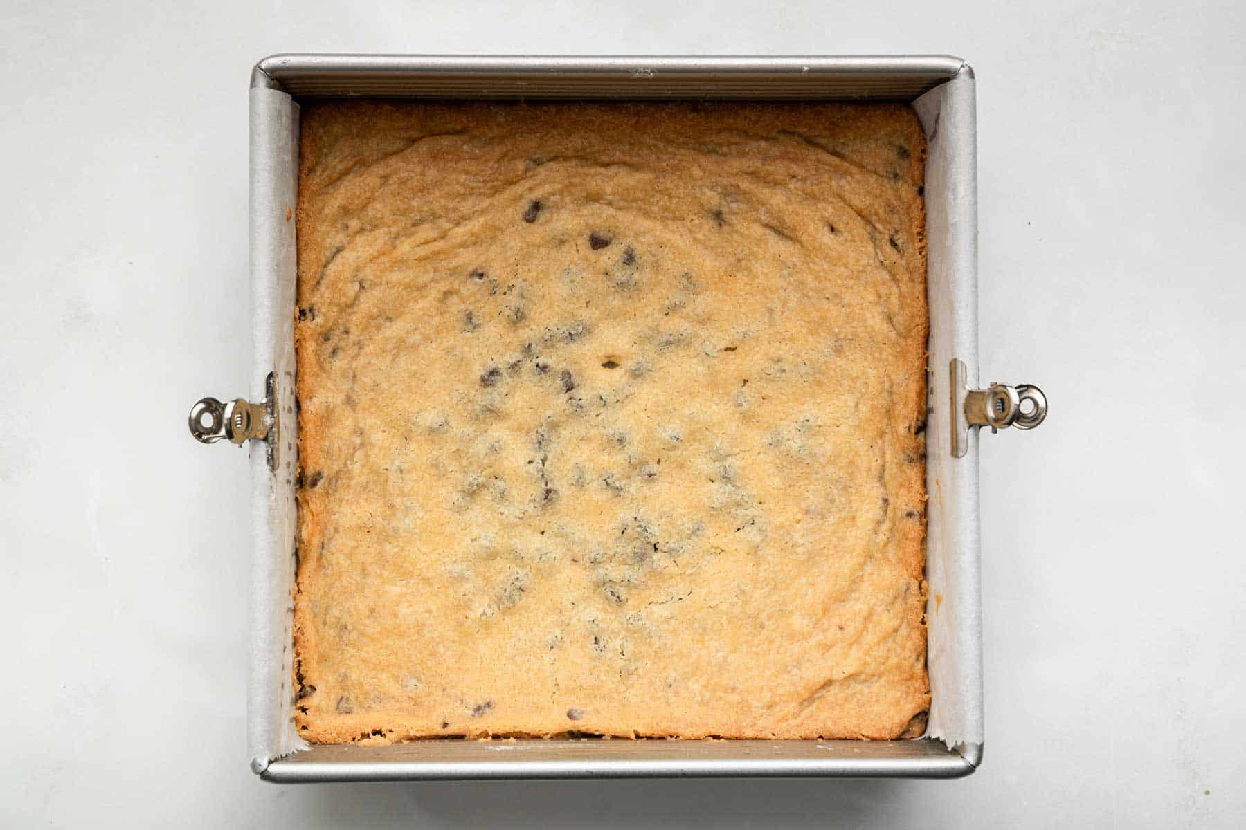 Golden brown chocolate chip cookie bars in a square pan.
