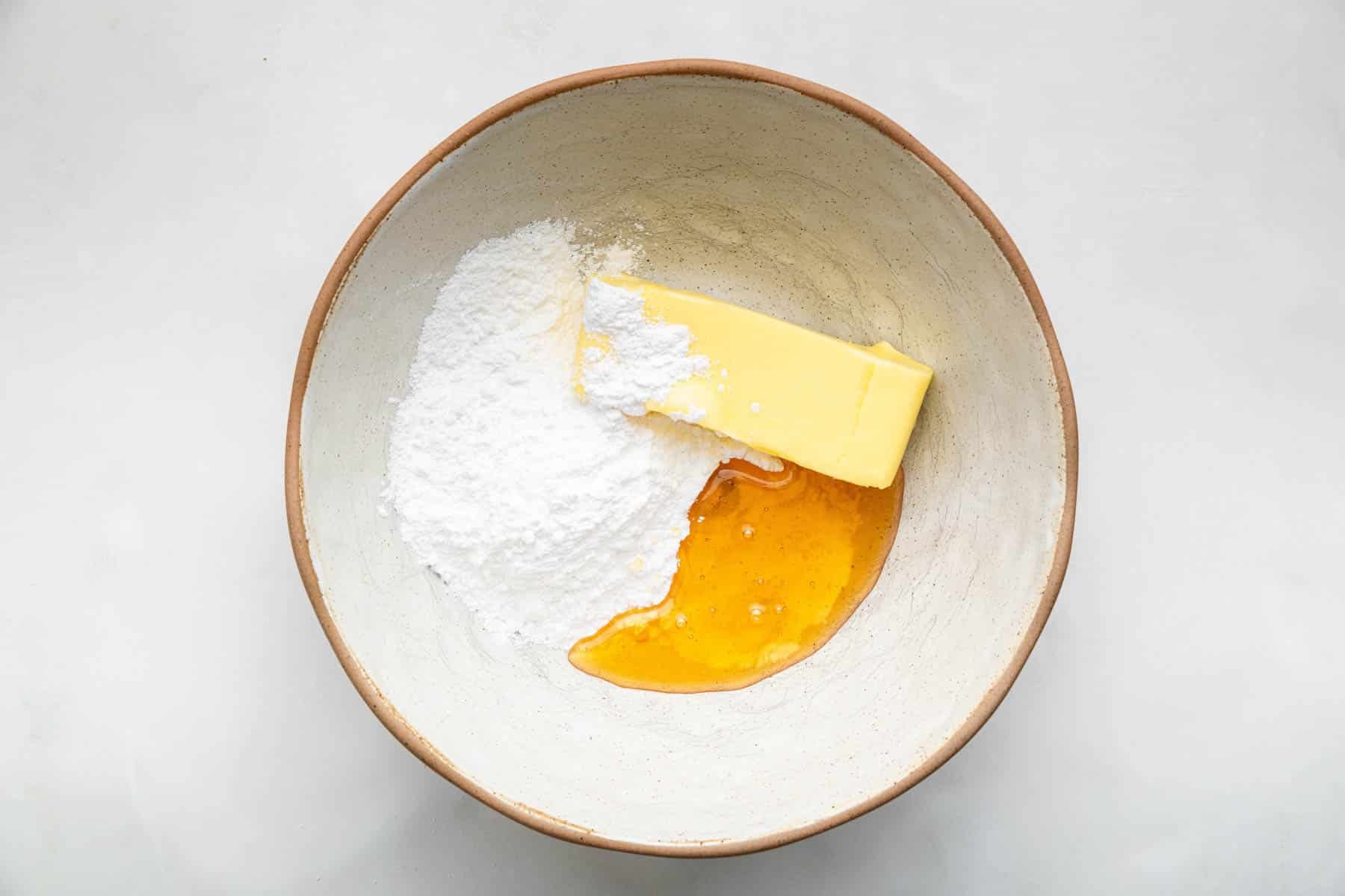 Bowl with a stick of butter, powdered sugar, and honey in it.