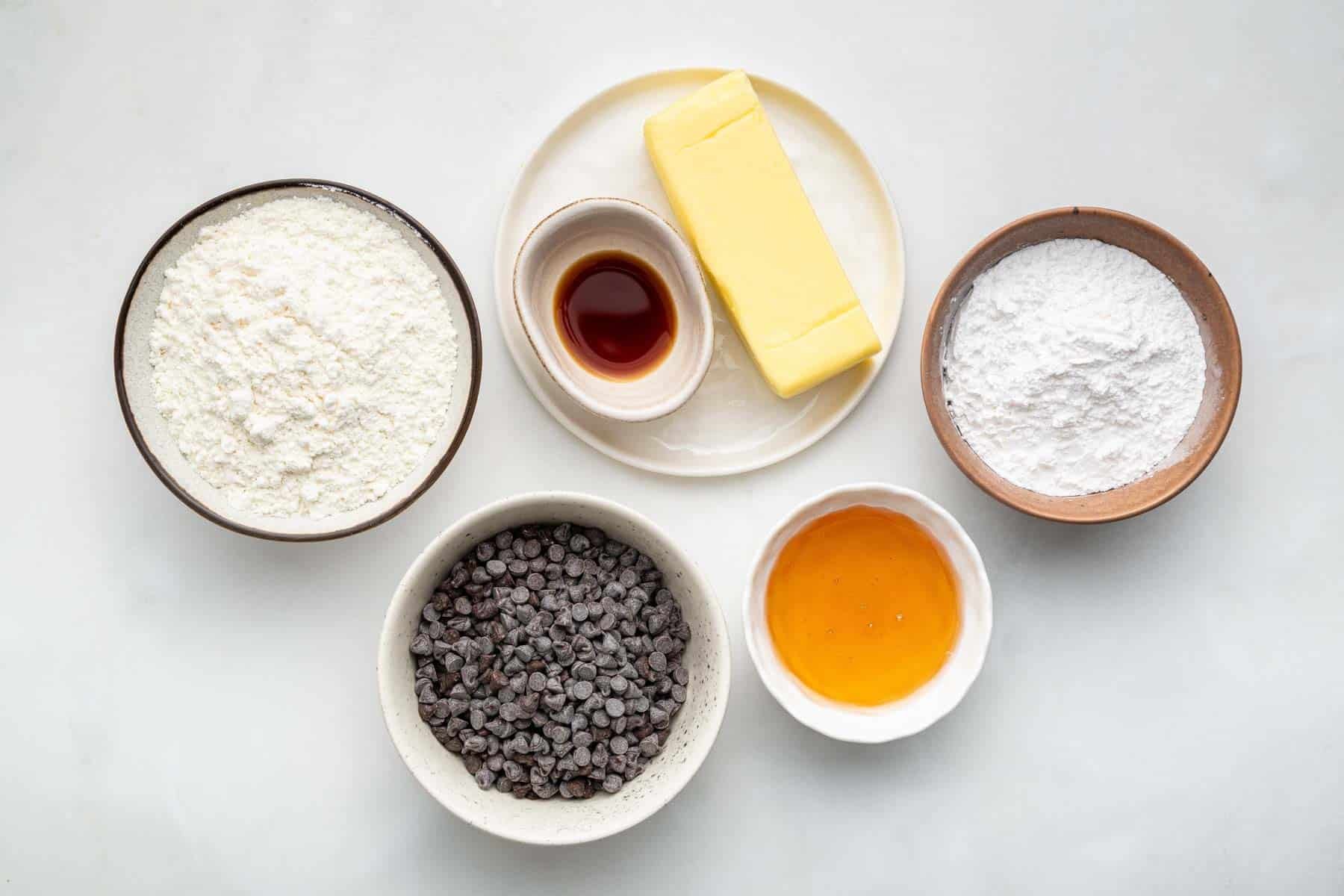 Bowl of flour, honey, vanilla, and stick of butter on kitchen counter.