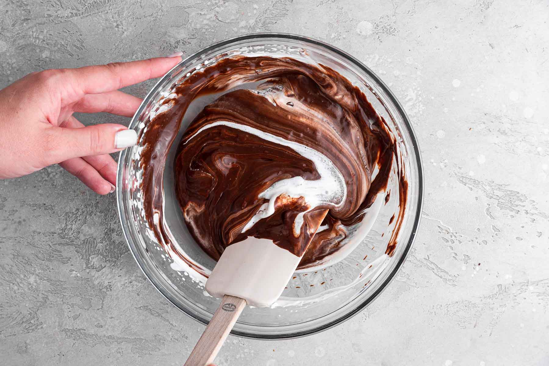 Hands folding white and dark brown desserts together in one bowl.