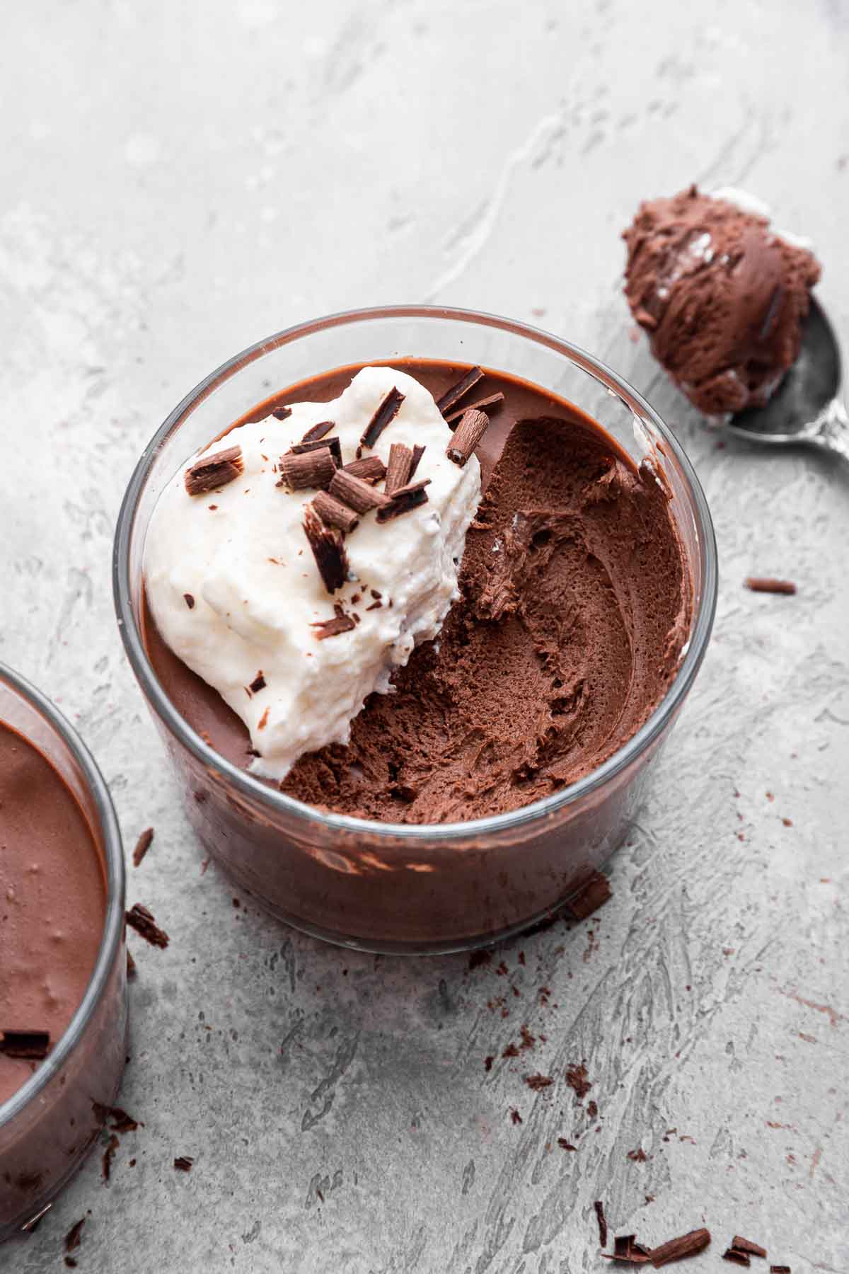 Two glasses of chocolate mousse with bite removed and whipped cream on side.