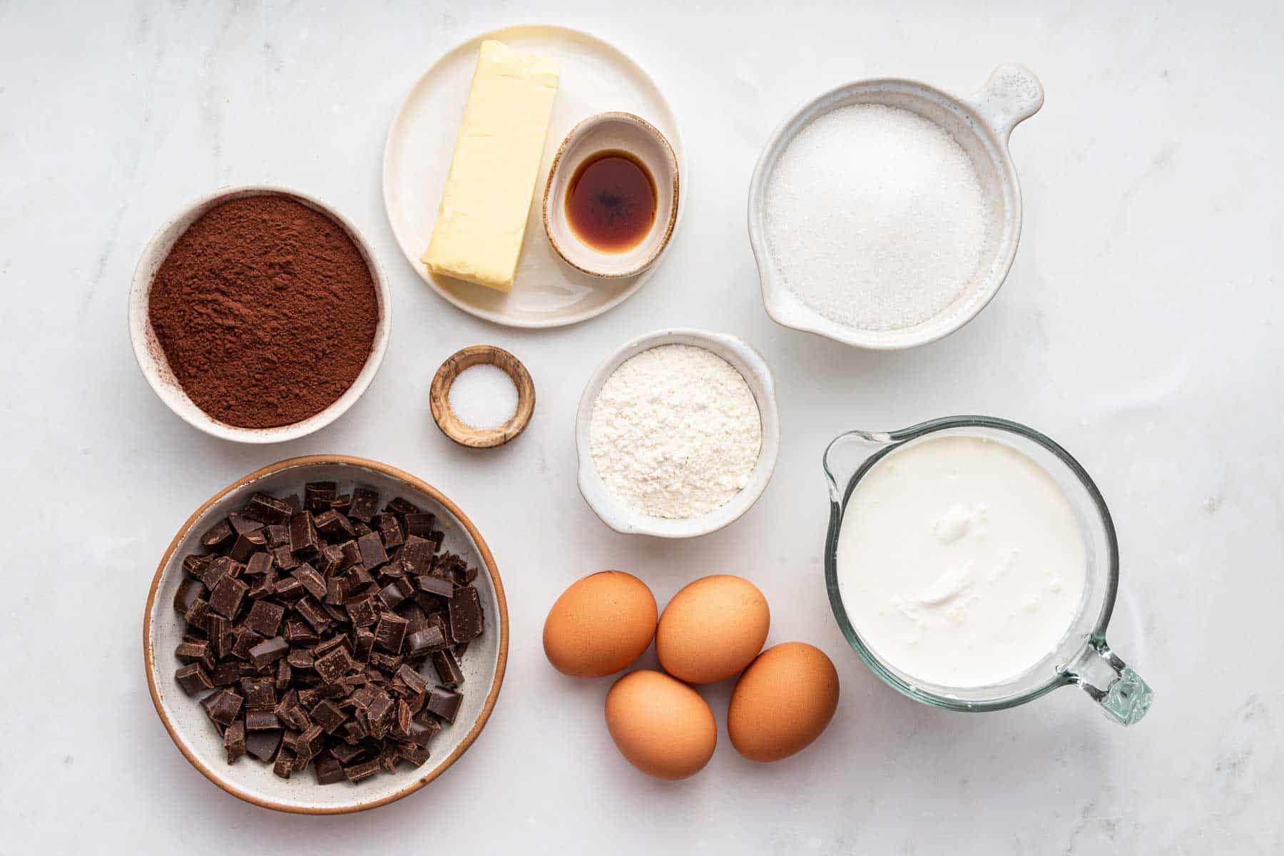 Bowl of cocoa powder, four eggs, sugar, butter and flour on counter.