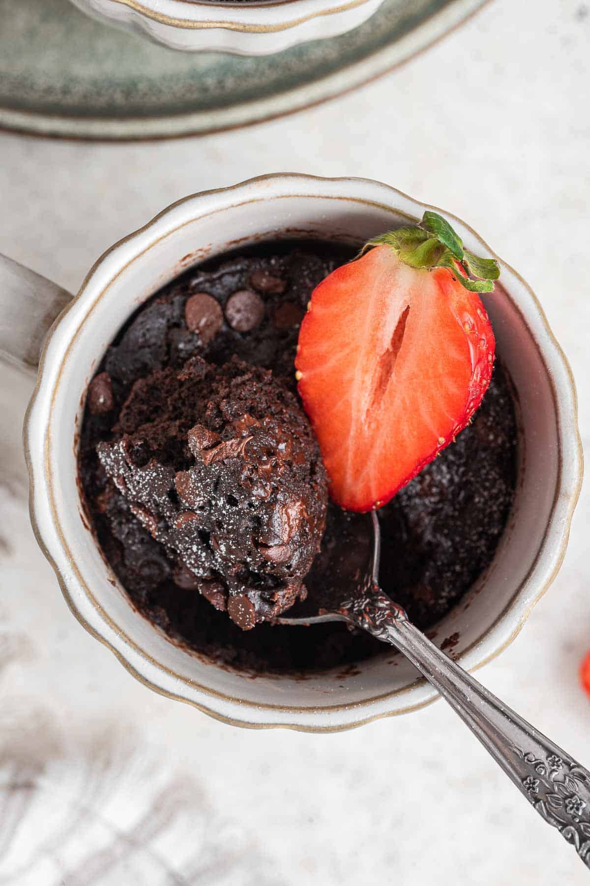Close up of chocolate mug cake with bite on spoon and strawberry on top.