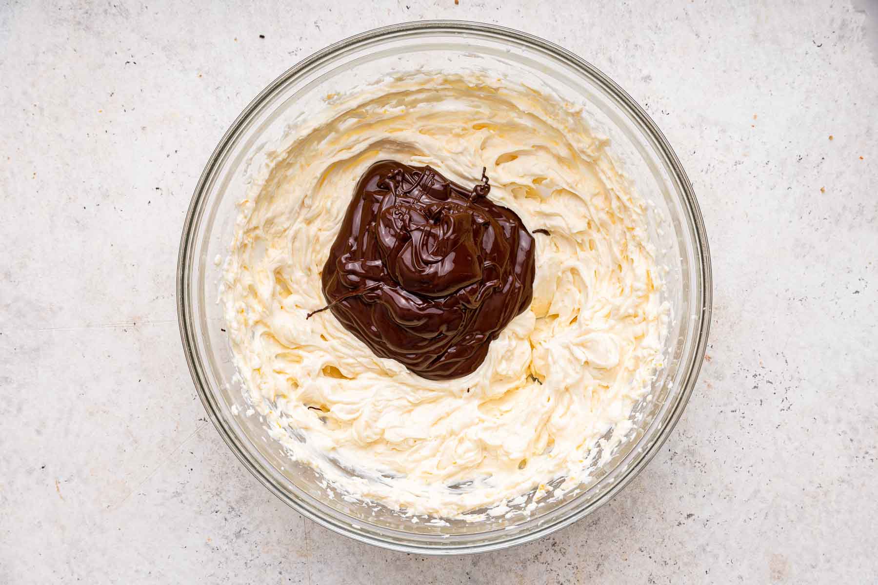 Whipped cream with melted chocolate poured on top, waiting to be folded together.