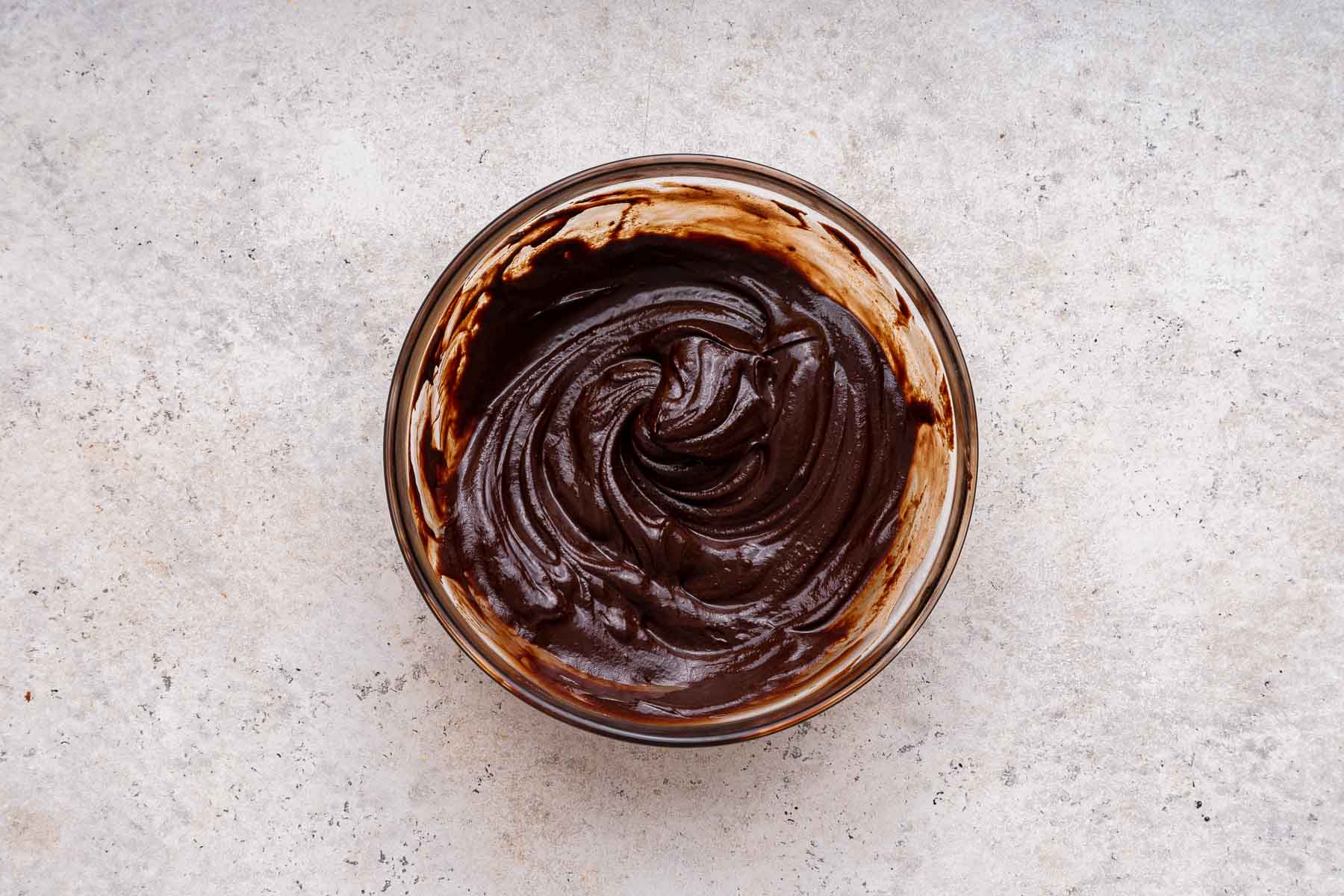 Melted semisweet chocolate in a clear glass bowl on grey marble counter.