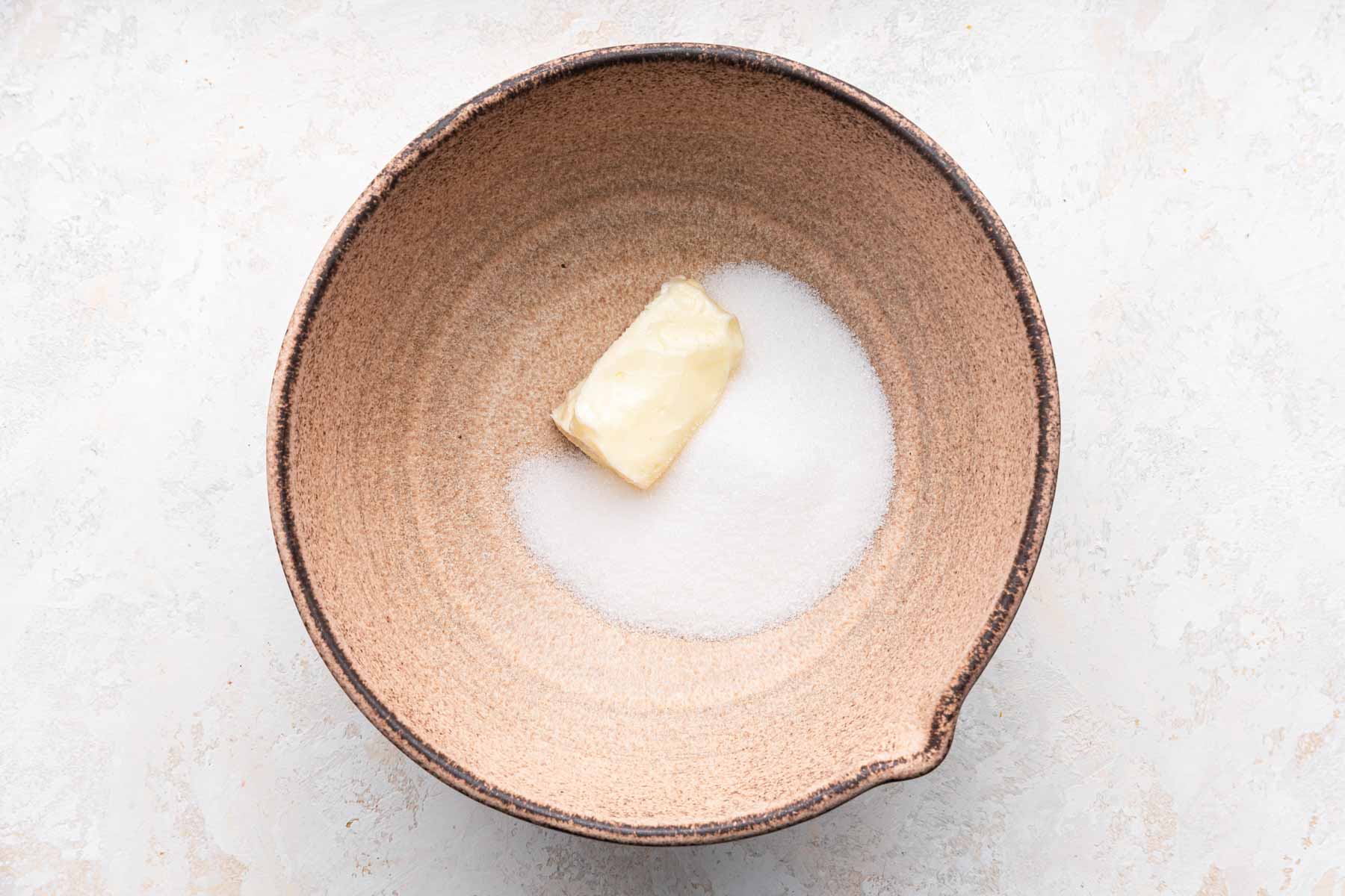Brown bowl with half a stick of butter and granulated sugar.
