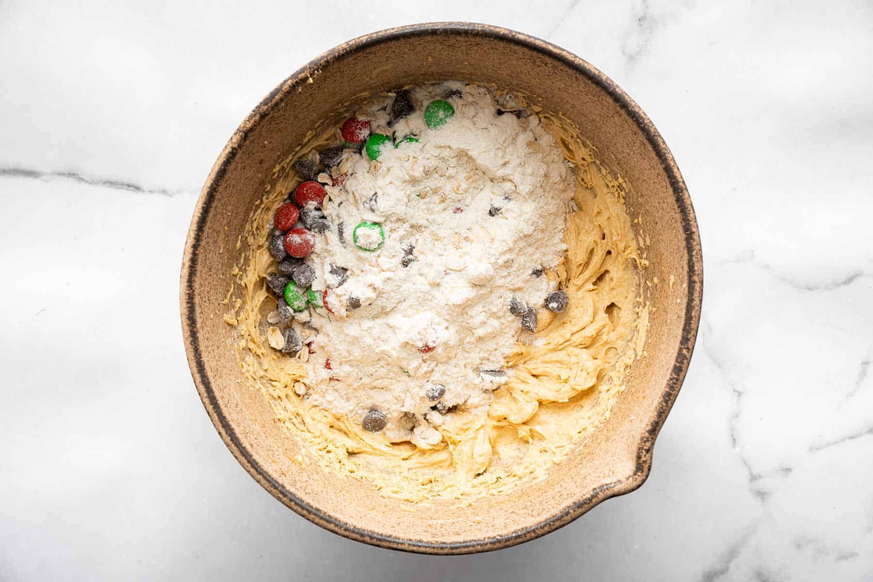 Flour and oats with colorful sprinkles on top of tan whipped batter in bowl.