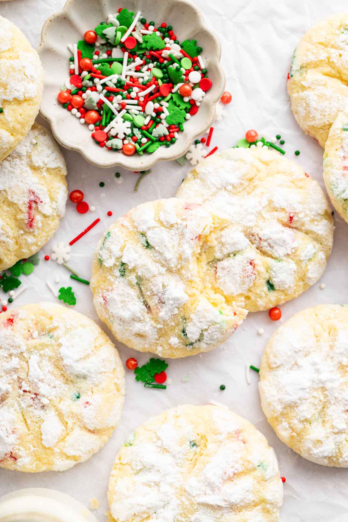 Overhead shot of christmas ooey gooey butter cookies with bowl of sprinkles on side.