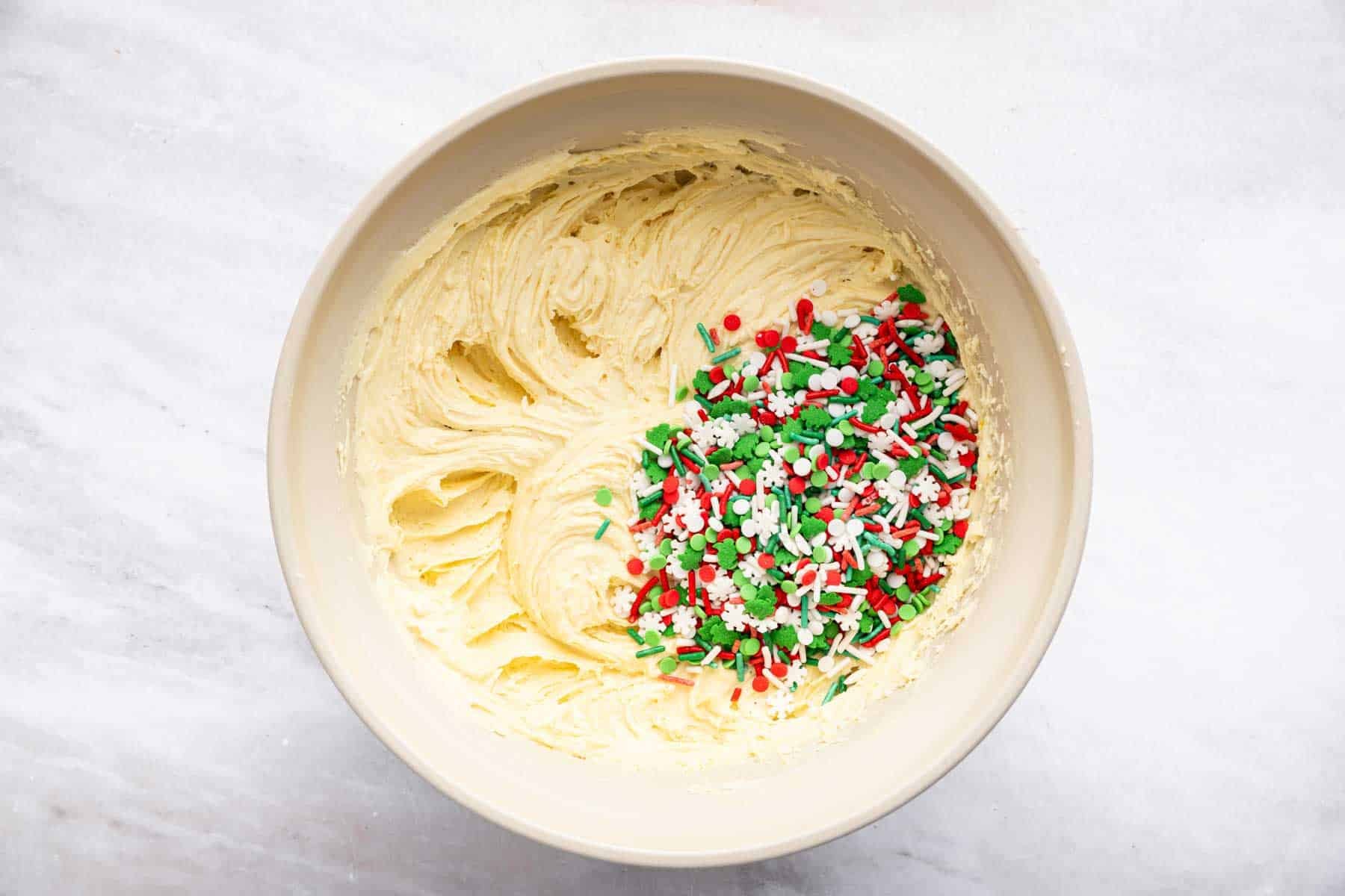 Holiday sprinkles on top of yellow batter in a bowl.